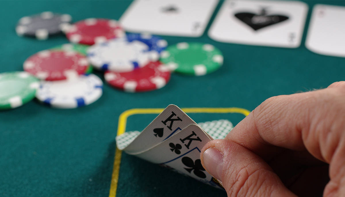 Playing Cards 桌布 壁紙 — 一隻手拿著兩張黑桃和梅花K的特寫，背景是綠色賭桌，上面散落著彩色籌碼。