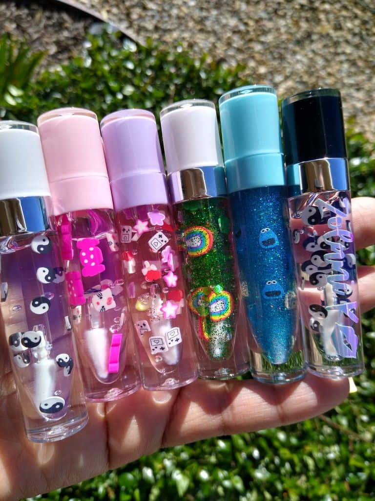 lipstick 桌布 壁紙 — 一隻手拿著六個色彩繽紛的亮粉膠水瓶，帶有漂浮的飾物，背景是綠色戶外。