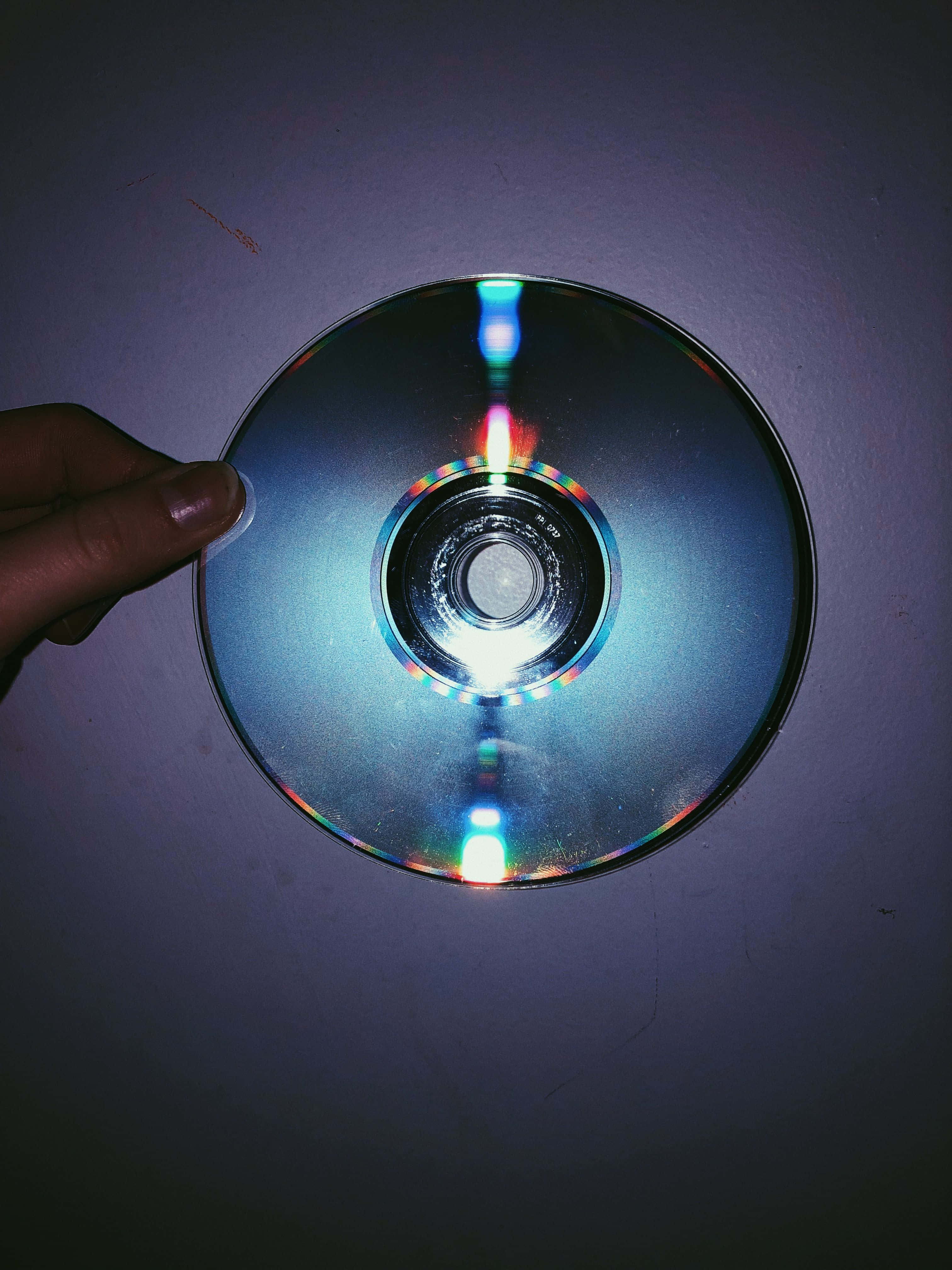 美學 桌布 壁紙 — 一隻手拿著反光的CD靠在昏暗的紫色牆上，在情緒化的特寫中捕捉到色彩繽紛的光暈。