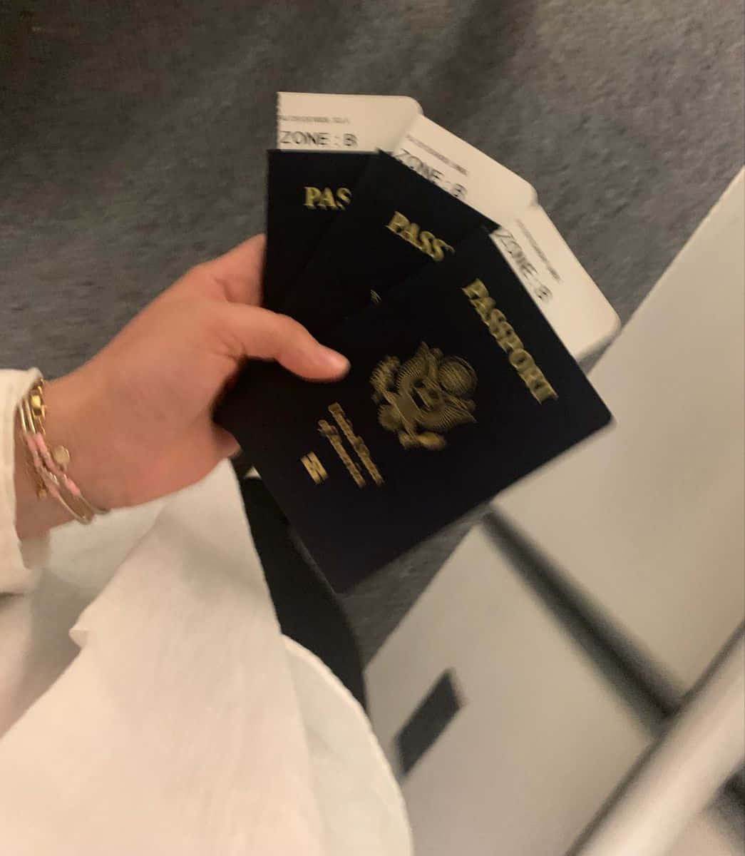 Passport 桌布 壁紙 — 一隻手拿著多本美國護照和登機證，背景是模糊的機場閘口。