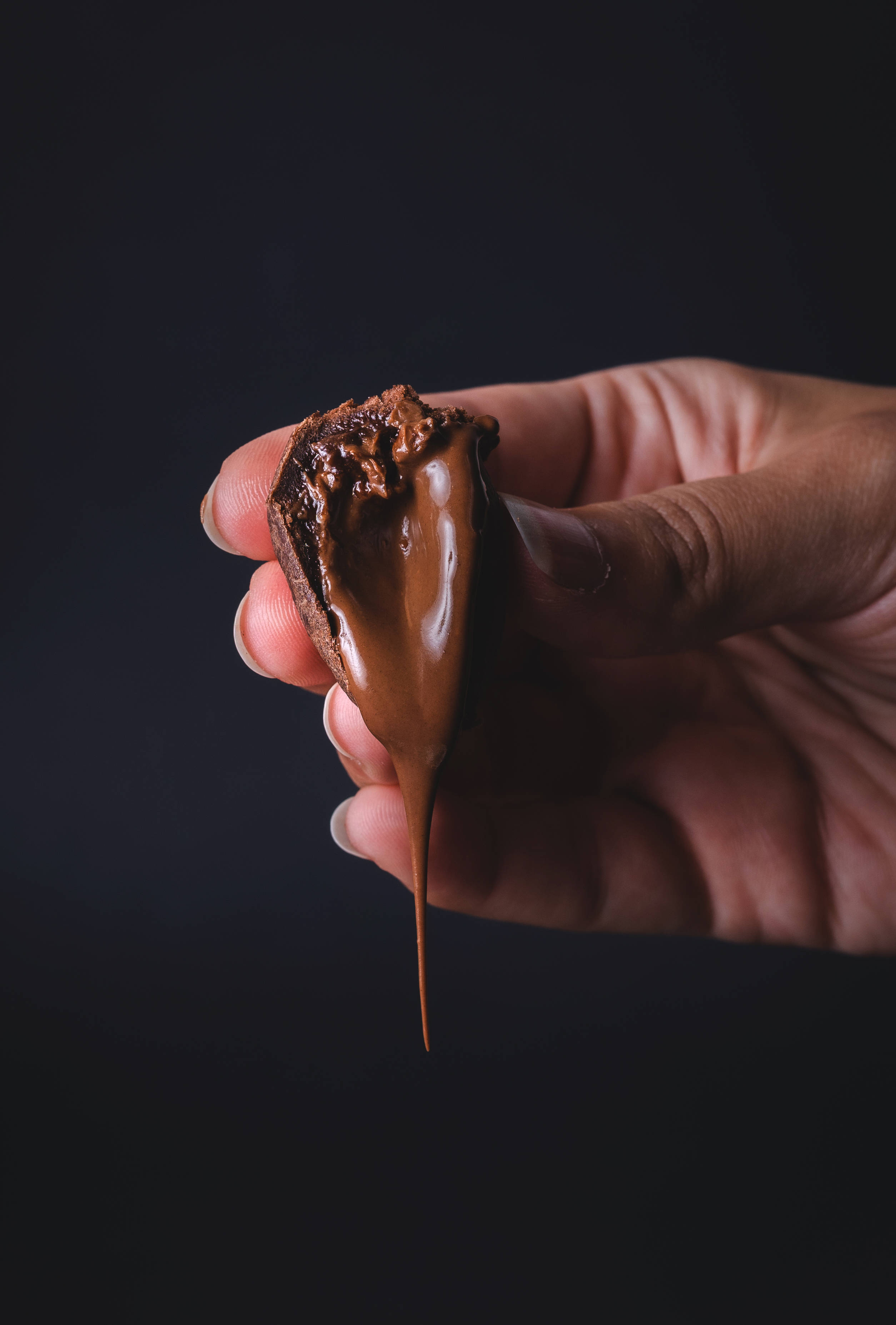 Chocolate 桌布 壁紙 — 一隻手拿著巧克力包裹的零食，濃郁的融化巧克力在深色背景下緩慢滴落。