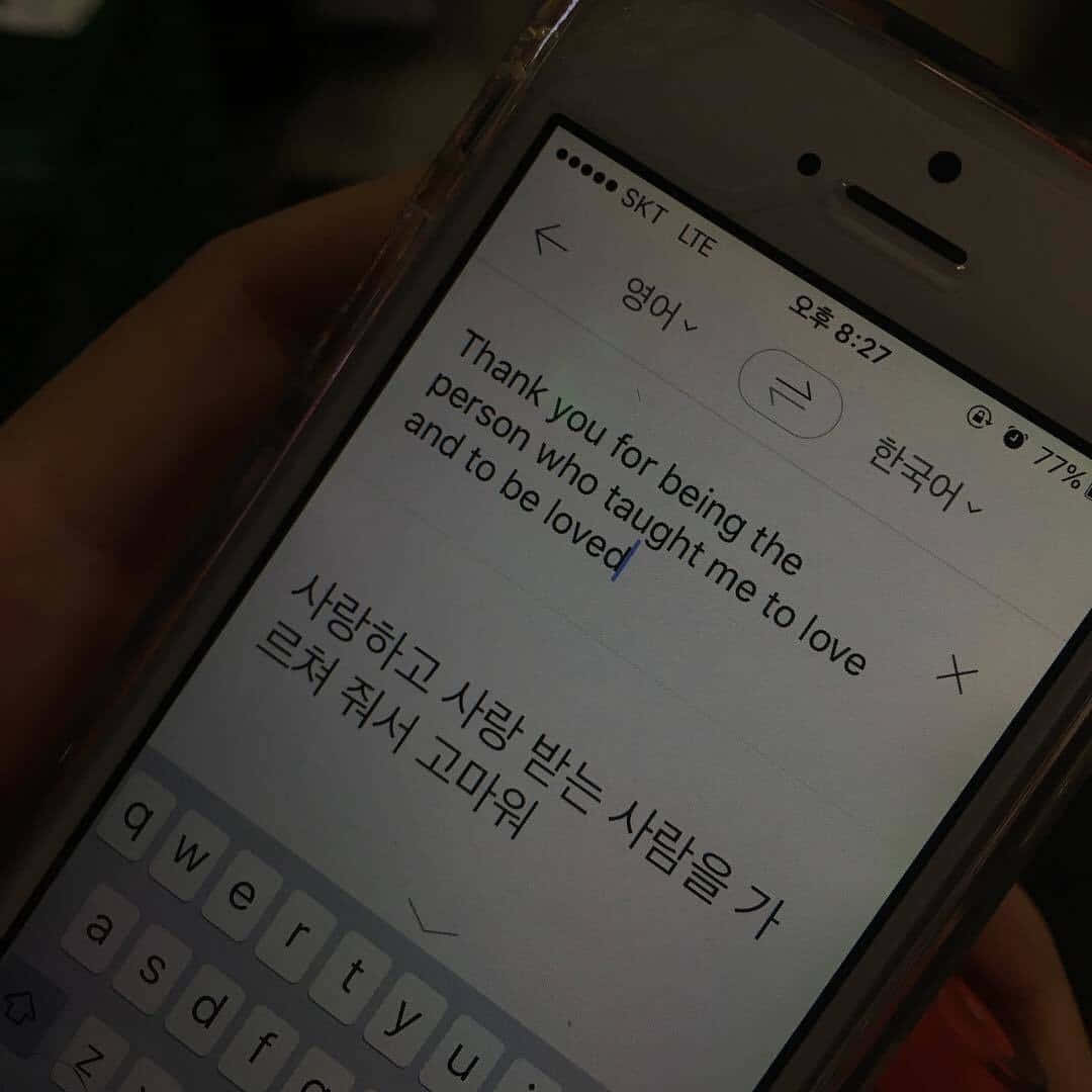 暗黑風格 桌布 壁紙 — 一隻手拿著手機，顯示一條溫馨的雙語訊息，感謝某人在昏暗燈光下教導愛。