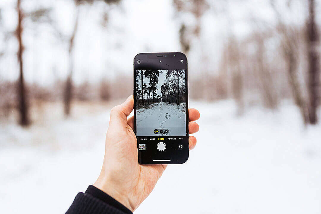 photography iPhone 桌布 壁紙 — 一隻手拿著智慧型手機，透過相機鏡頭捕捉雪地森林小徑。