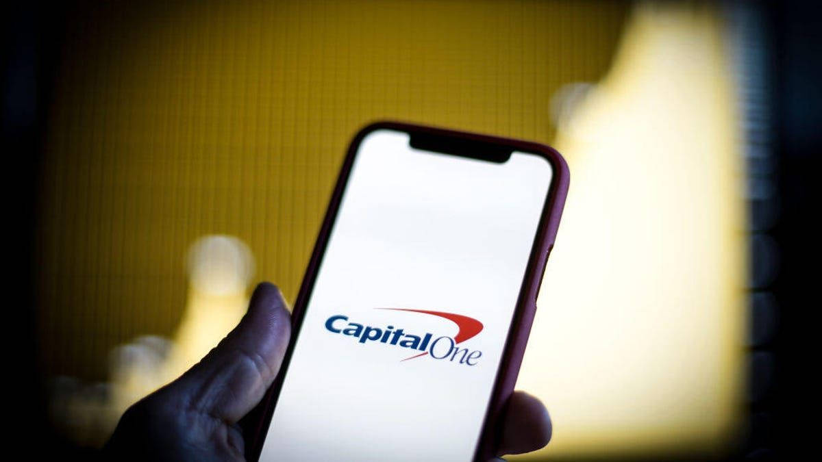 Phone Screen 桌布 壁紙 — 一隻手拿著智慧型手機，顯示Capital One標誌，背景溫暖模糊。