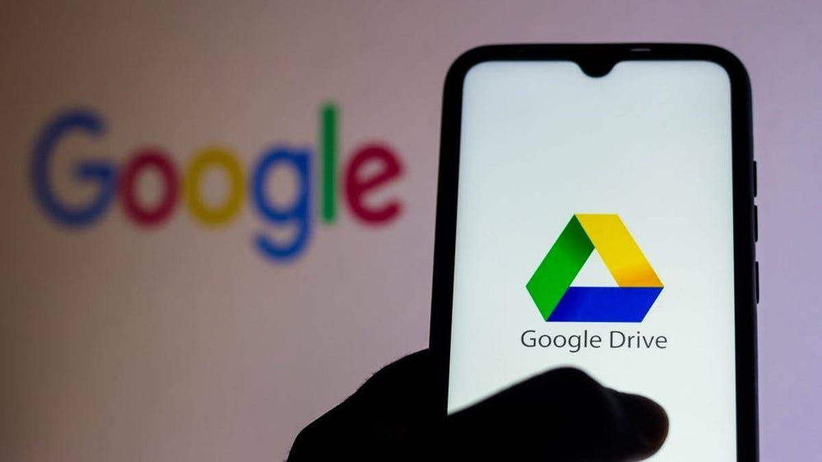 Software 桌布 壁紙 — 一隻手拿著智慧型手機，顯示Google Drive標誌，背景有模糊的Google標誌。
