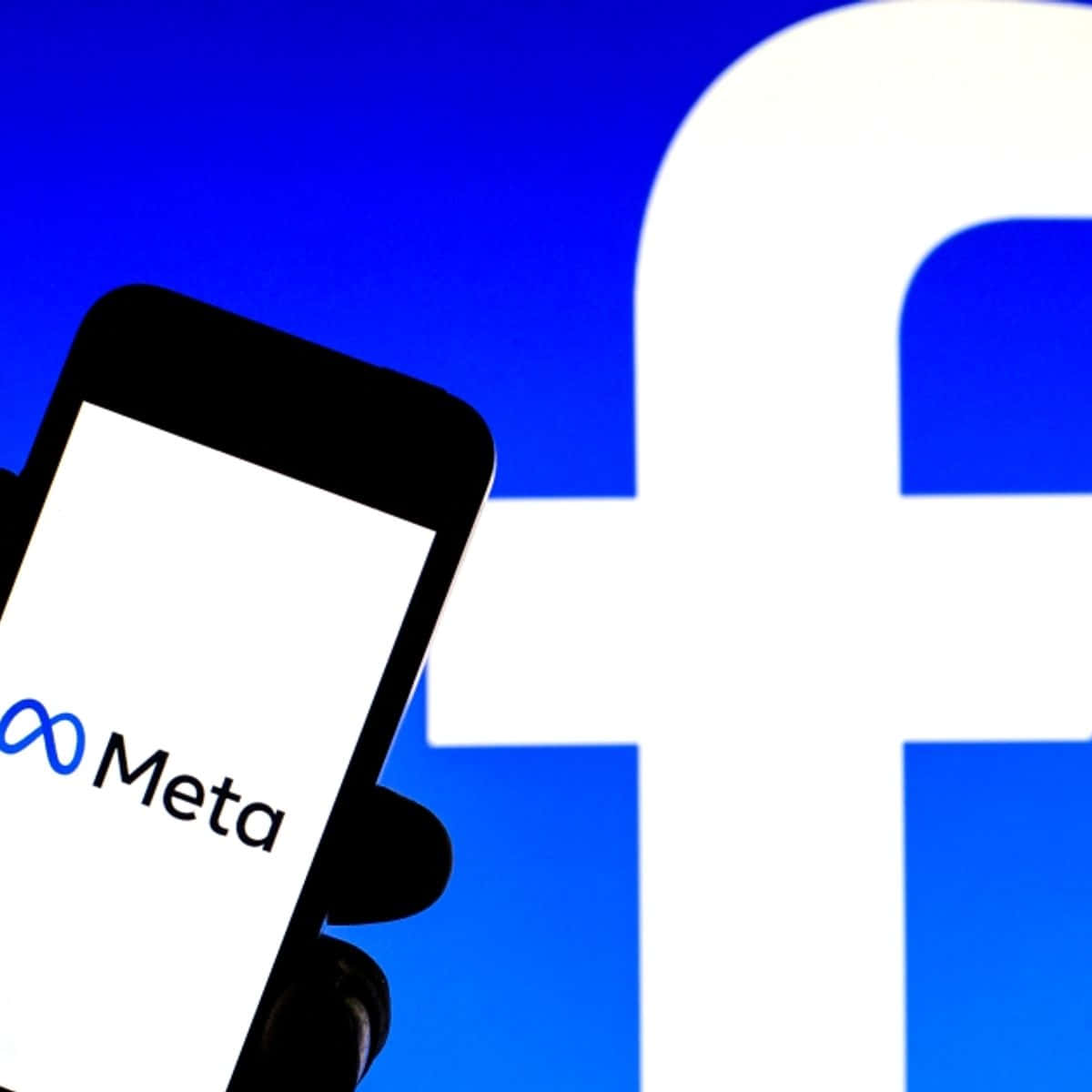 Facebook 桌布 壁紙 — 一隻手拿著智慧型手機，顯示Meta標誌，背景是大型藍色Facebook 'f'標誌。