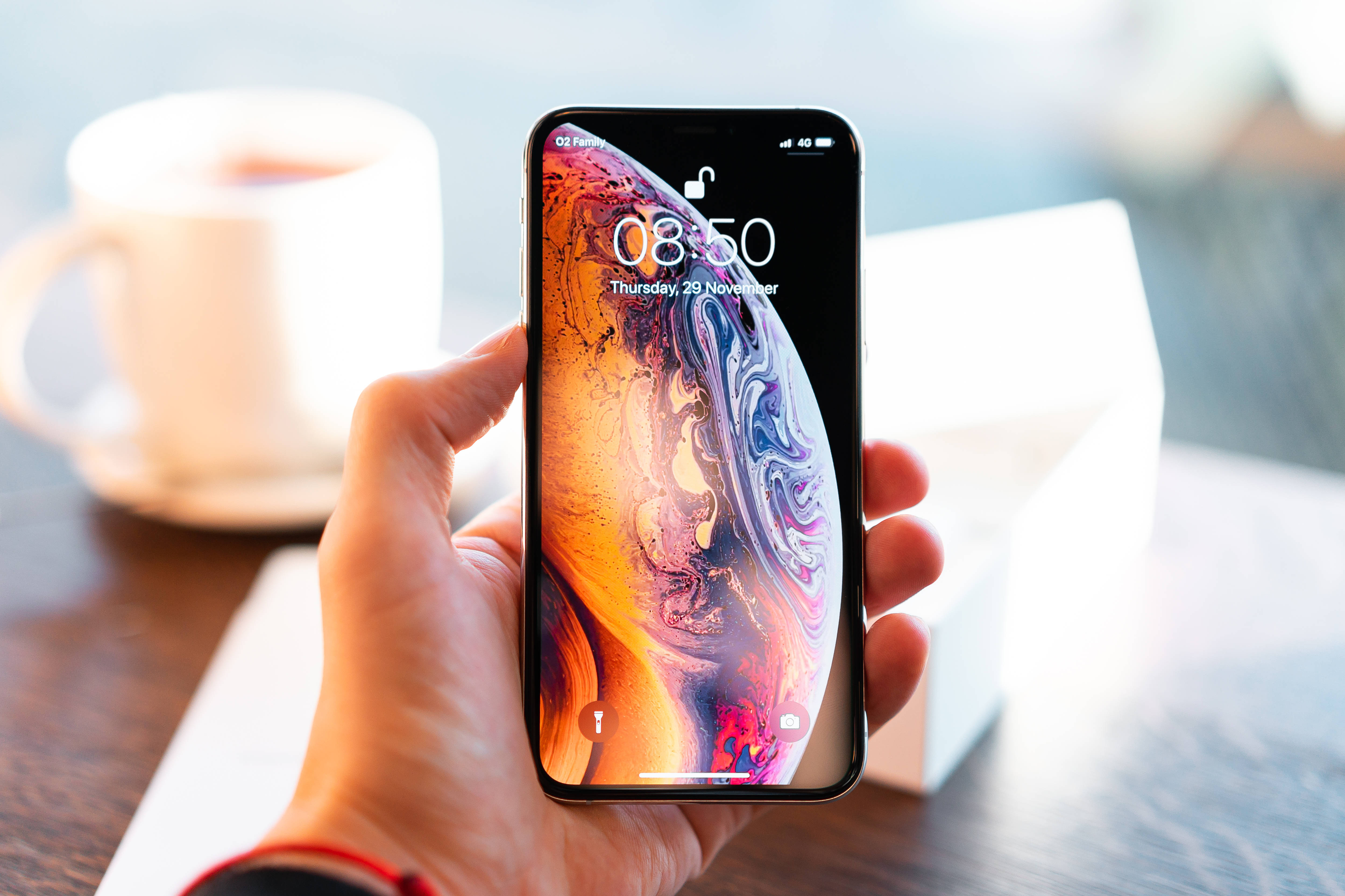 Screen 桌布 壁紙 — 一隻手拿著智慧型手機，顯示一個充滿活力的旋轉抽象桌布，背景中有一杯模糊的咖啡。