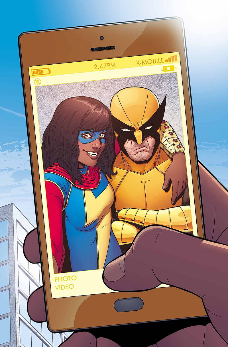 Ms Marvel 桌布 壁紙 — 一隻手拿著智慧型手機，顯示一張漫畫風格的照片，照片中有一位微笑的女子穿著藍黃色服裝，還有一位嚴肅的黃色面具男子，背景是城市景觀。