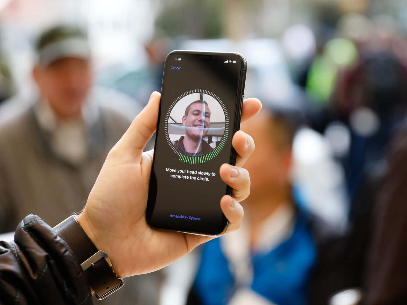 Face Id 桌布 壁紙 — 一隻手拿著智慧型手機，顯示人臉辨識設定畫面，上面有一個微笑的男士臉孔和指示緩慢移動頭部。