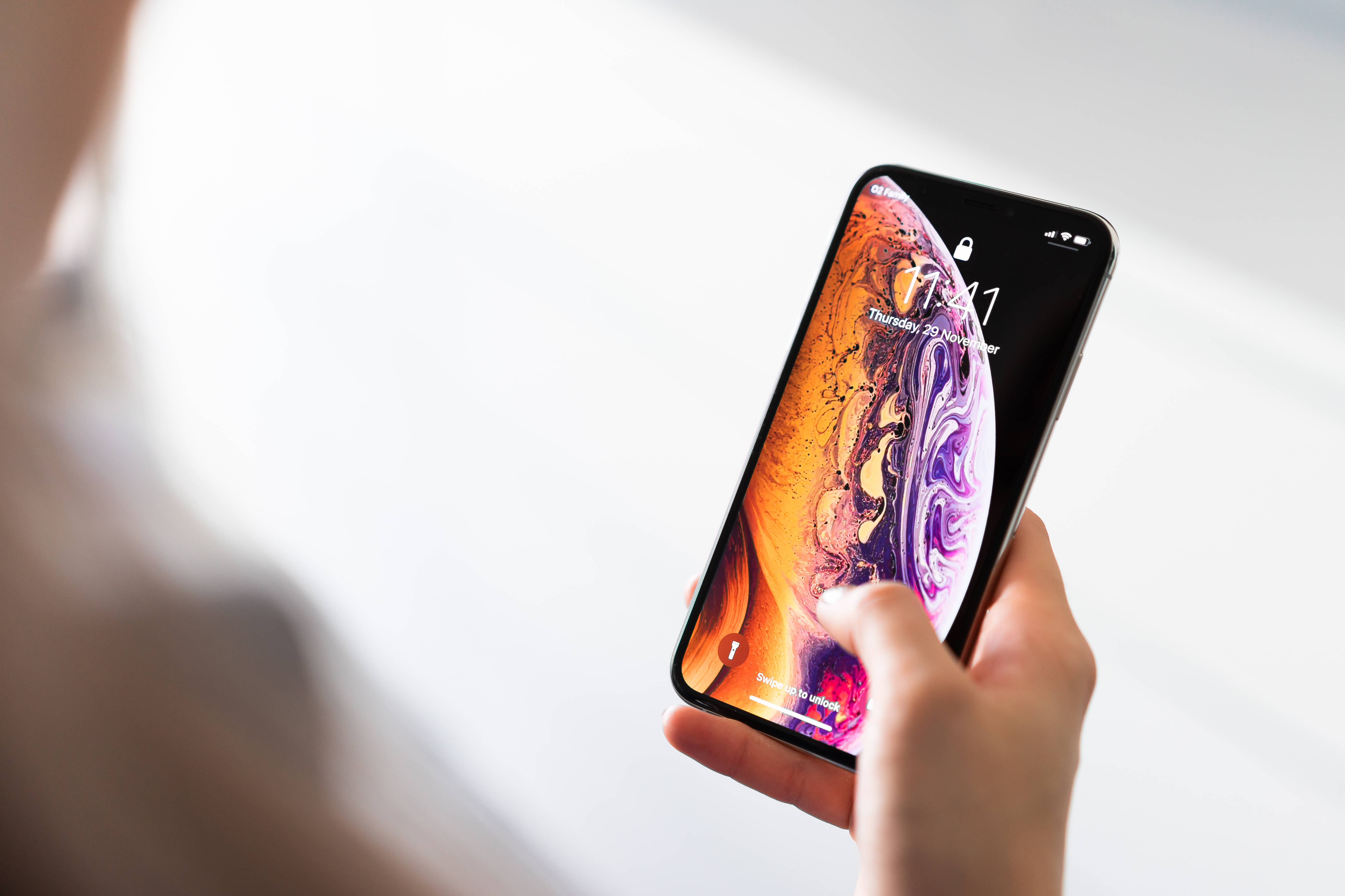 Screen 桌布 壁紙 — 一隻手拿著智慧型手機，顯示充滿活力的旋轉抽象桌布，帶有橙色、紫色和粉紅色調。