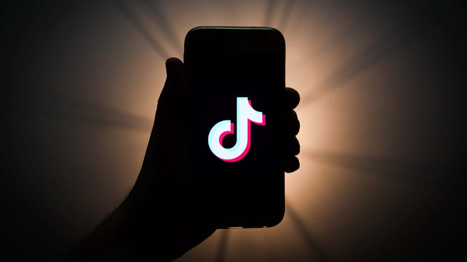 TikTok Logo 桌布 壁紙 — 一隻手拿著智慧型手機，顯示發光的TikTok標誌，背景是耀眼的光線。