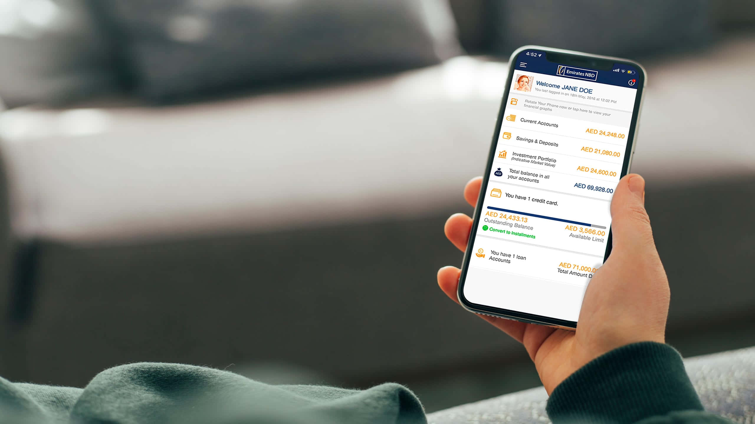 Mobile Banking 桌布 壁紙 — 一隻手拿著智慧型手機，顯示銀行應用程式，包含帳戶餘額和財務詳細資訊，背景是模糊的沙發。