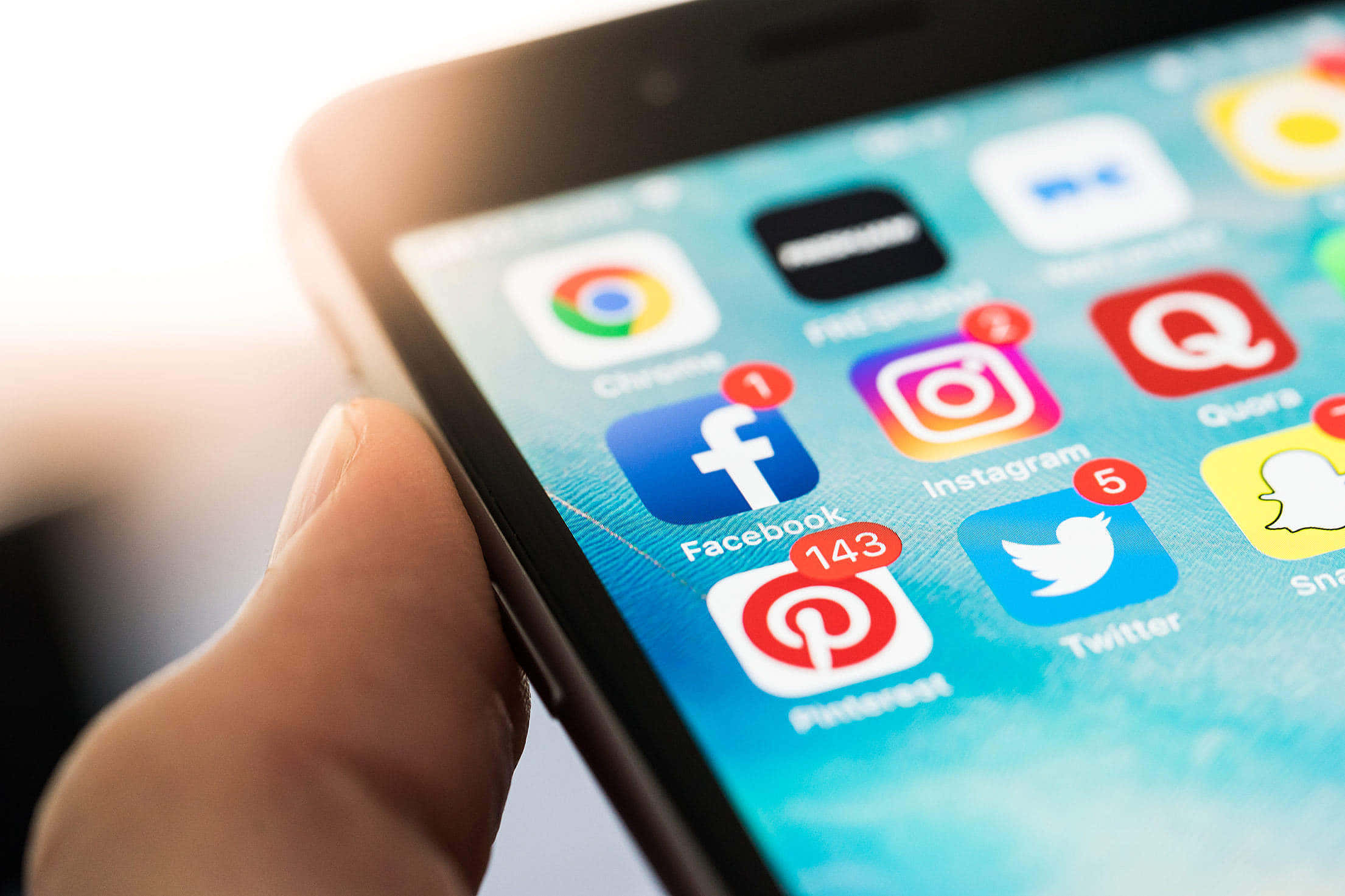 Social Media 桌布 壁紙 — 一隻手拿著智慧型手機的特寫，顯示社交媒體應用程式圖示和通知徽章。