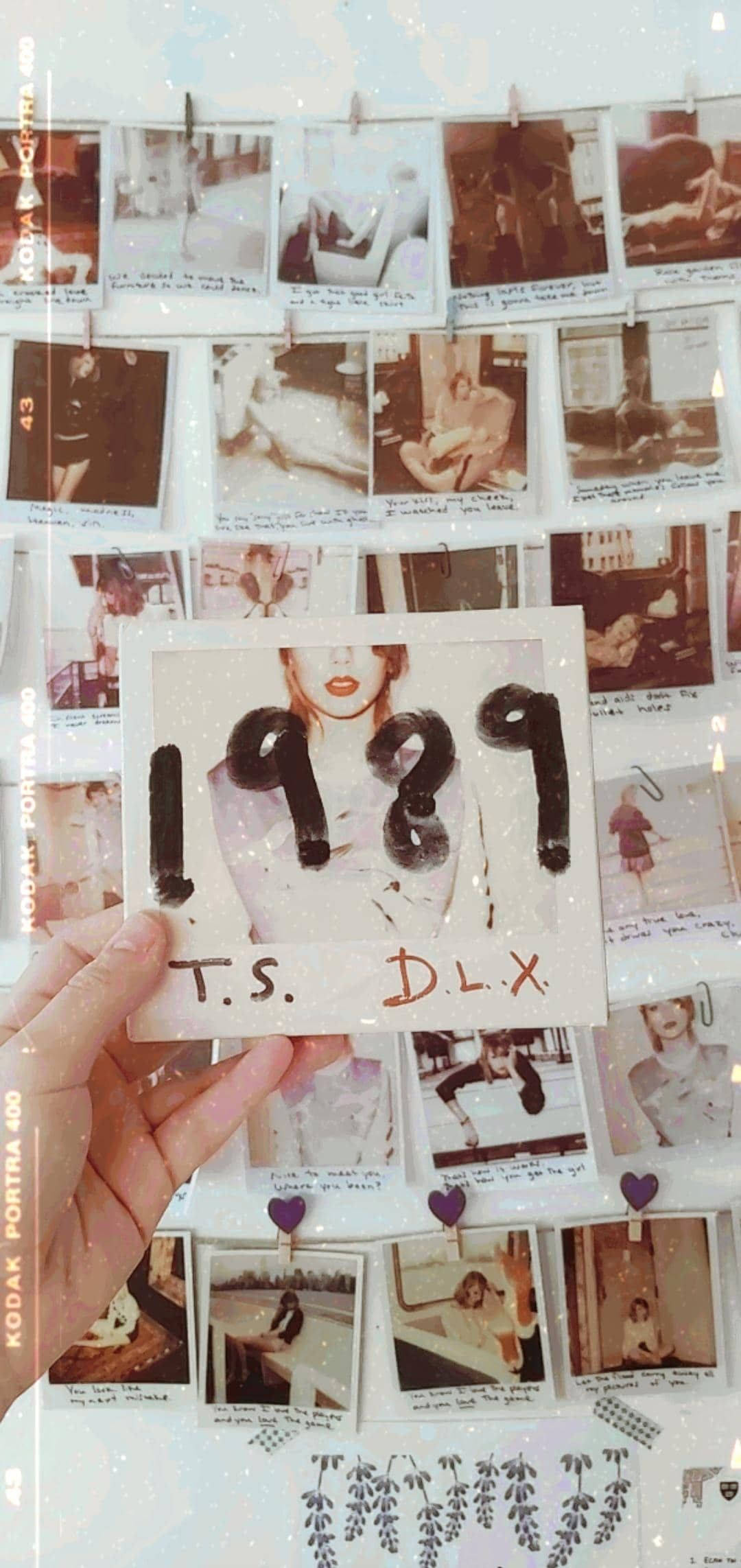 拍立得 桌布 壁紙 — 一隻手拿著標有1989 T.S. D.L.X.的拍立得照片，對著一面用紫色愛心別針固定復古照片的牆。