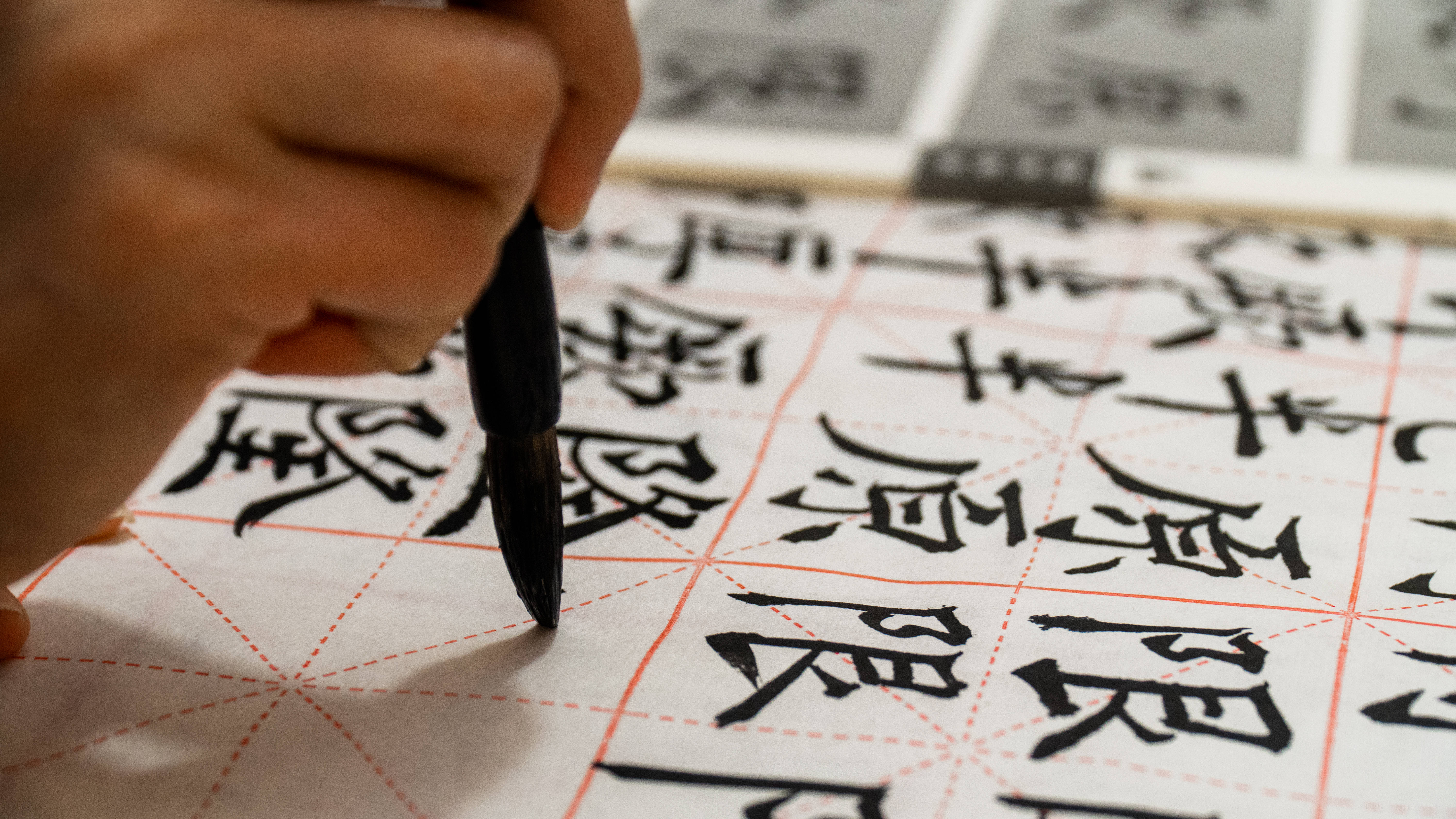中文 桌布 壁紙 — 一隻手拿著毛筆，懸在帶有粗體黑色漢字的格子米紙上。