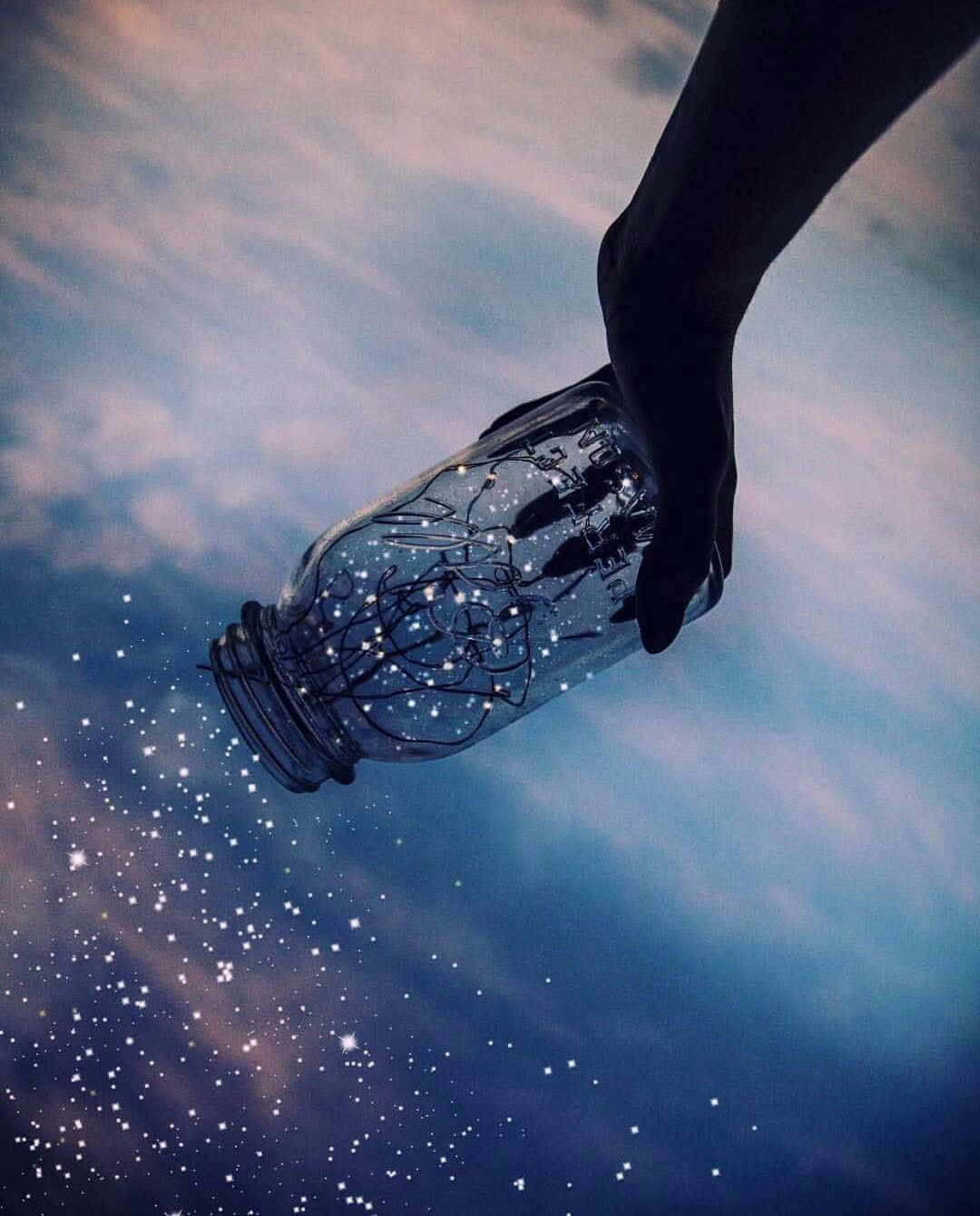 美學 桌布 壁紙 — 一隻手拿著玻璃罐，將星星倒入帶有薄雲的暮色天空中。