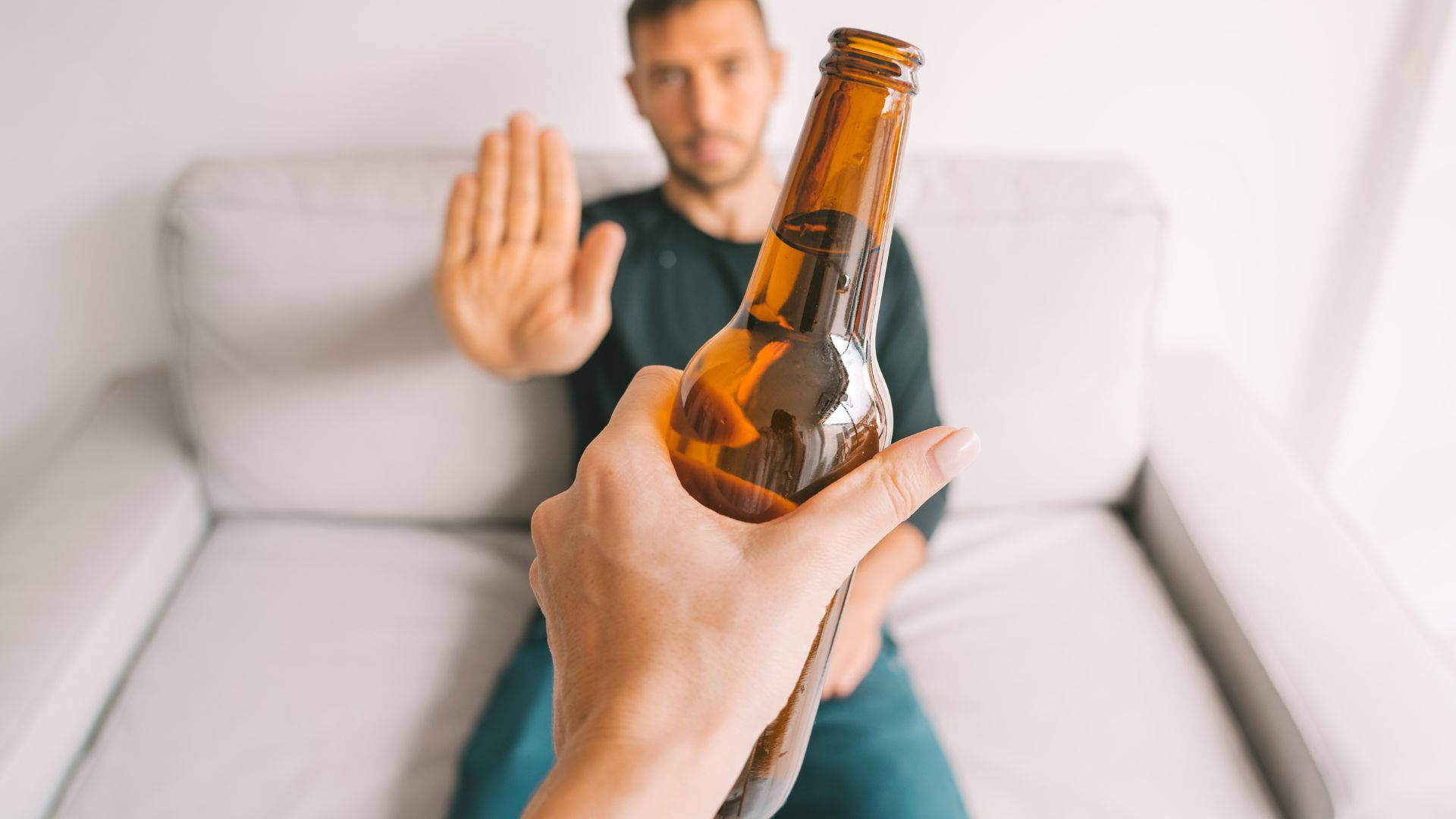 alcohol 桌布 壁紙 — 一隻手拿著琥珀色啤酒瓶，而沙發上的男人則堅決地做手勢制止。