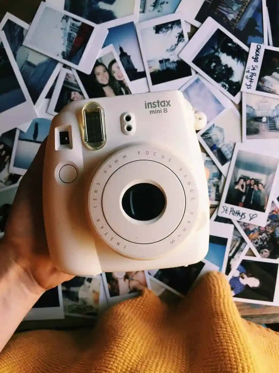 相機 桌布 壁紙 — 一隻手拿著白色Instax Mini 8相機，懸在散落的即時照片和手寫筆記上方。