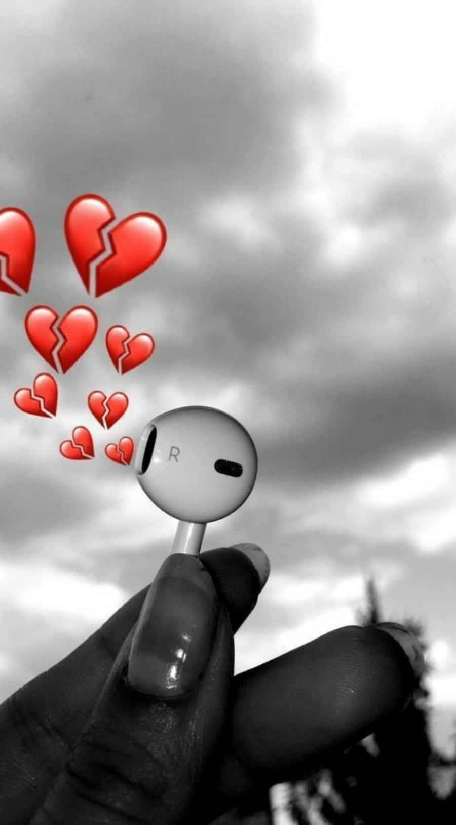 Broken Heart Sad 桌布 壁紙 — 一隻手拿著白色耳塞，背景是陰天，漂浮著紅色破碎心形表情符號。