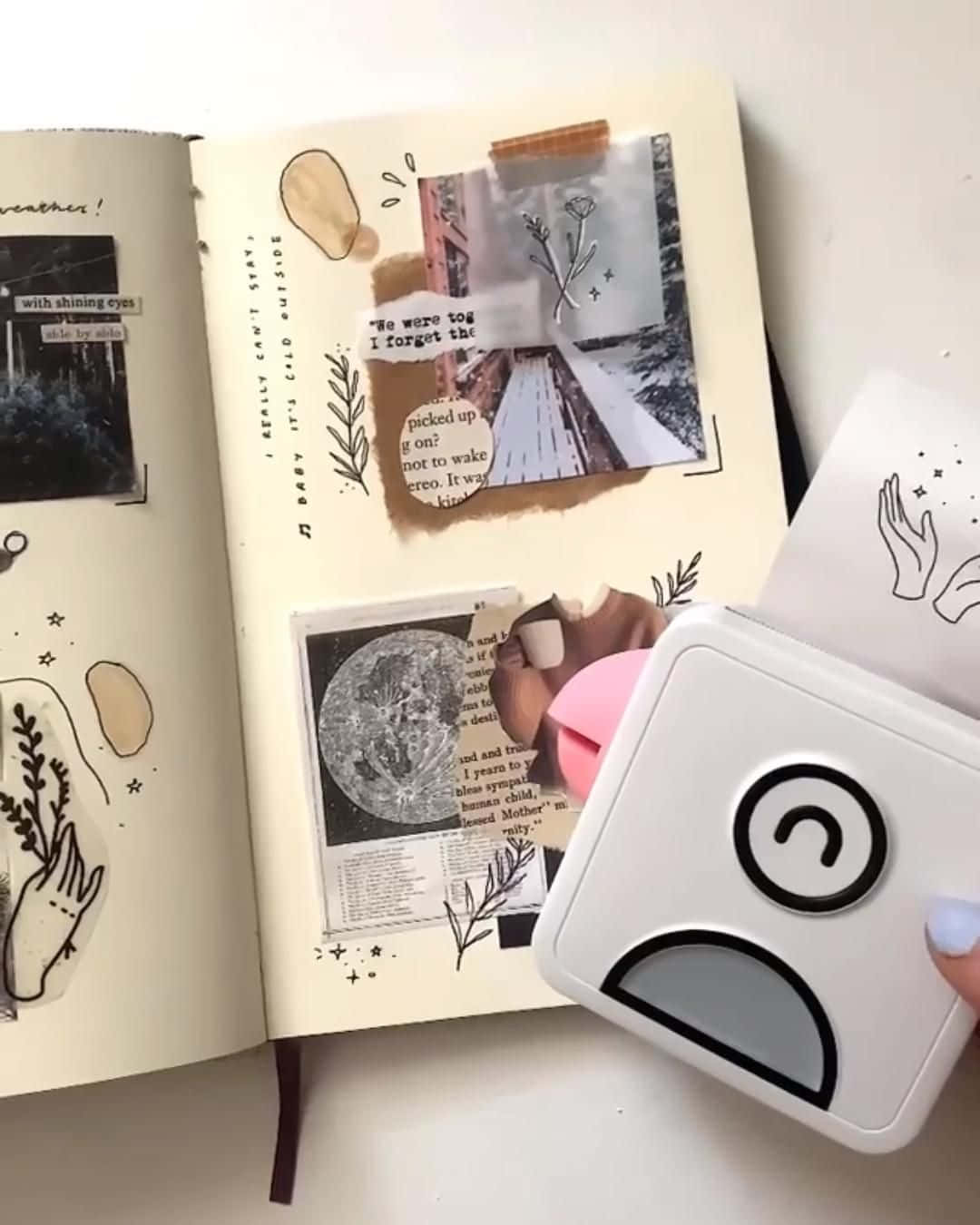 Scrapbooking 桌布 壁紙 — 一隻手拿著白色貼紙製造機，放在一個打開的剪貼簿上，裡面充滿了照片、語錄和植物塗鴉，紙張為奶油色。