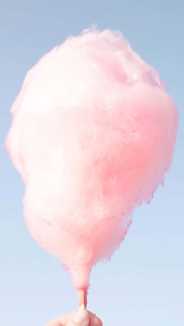Pink Cotton Candy 桌布 壁紙 — 一隻手拿著粉紅色棉花糖，背景是晴朗的藍天。