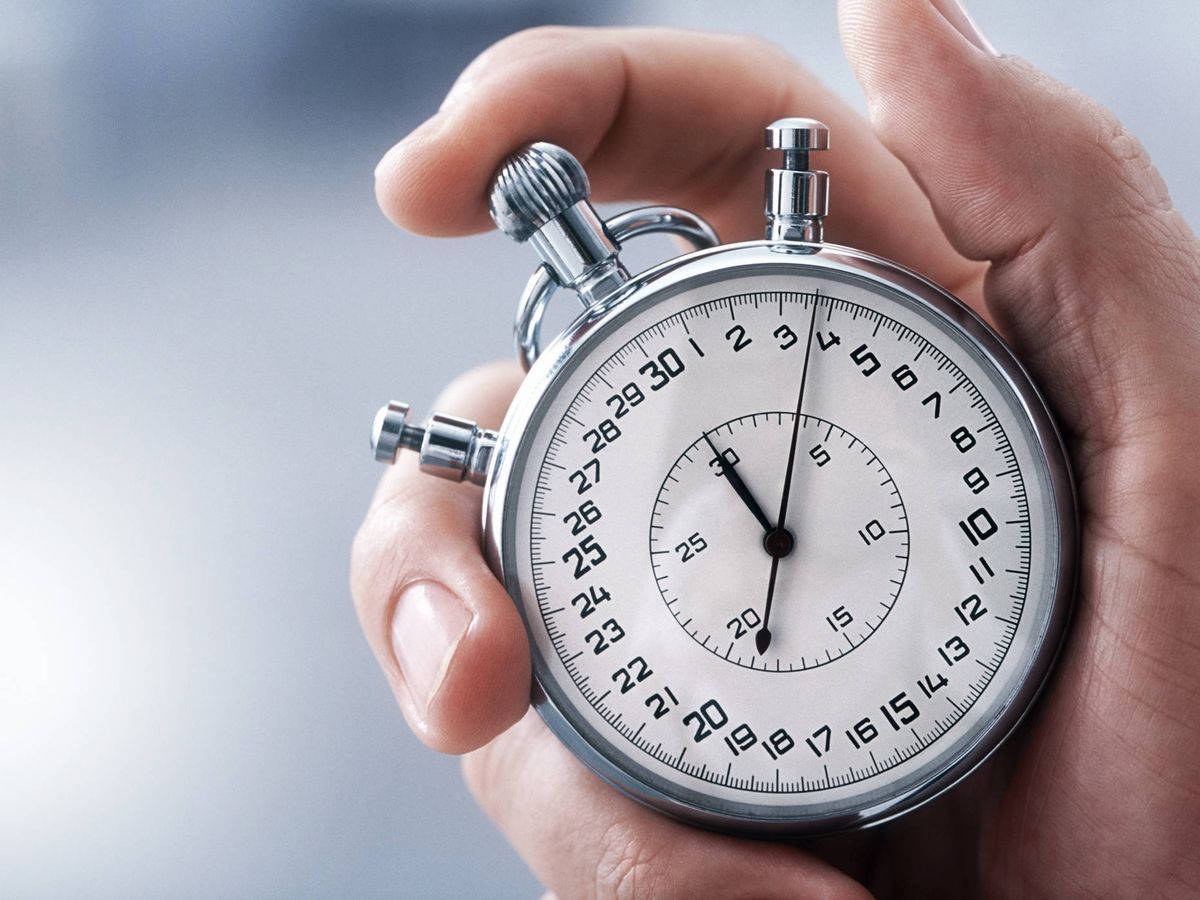 times up 桌布 壁紙 — 一隻手拿著經典的銀色碼錶，白色錶面配黑色數字，背景柔和模糊。