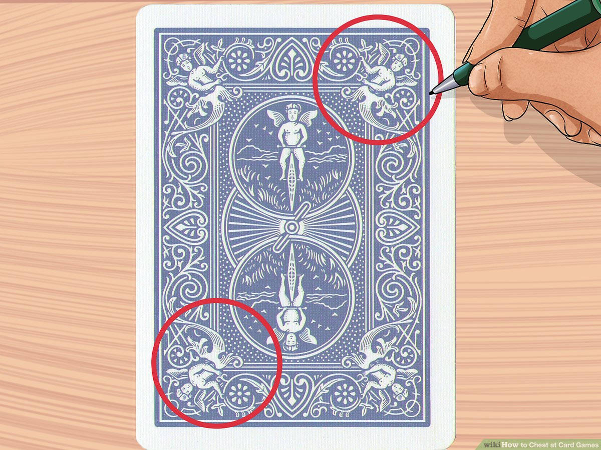 Playing Cards 桌布 壁紙 — 一隻手拿著綠色筆，指向木質表面上藍色撲克牌背面複雜的白色圖案。