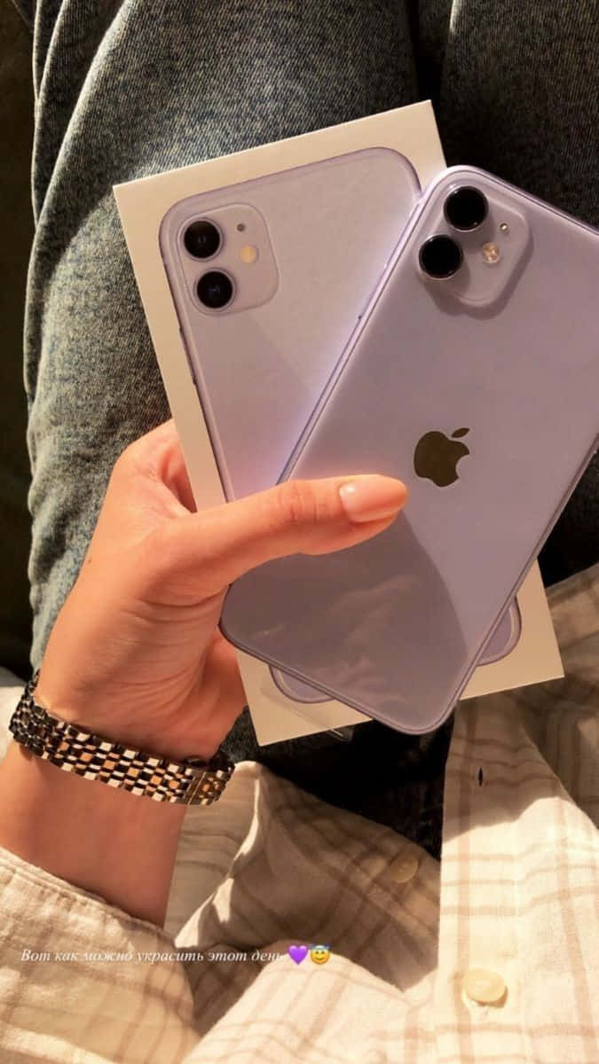 iPhone 12 桌布 壁紙 — 一隻手拿著薰衣草色 iPhone 11 Pro 及其盒子，背景是舒適的格紋襯衫和灰色布料。