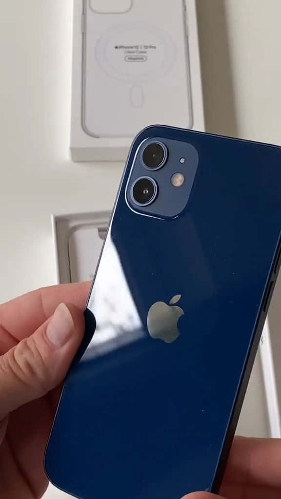 iPhone 12 桌布 壁紙 — 一隻手拿著藍色iPhone 12 mini，相機模組在白色盒子背景上可見。