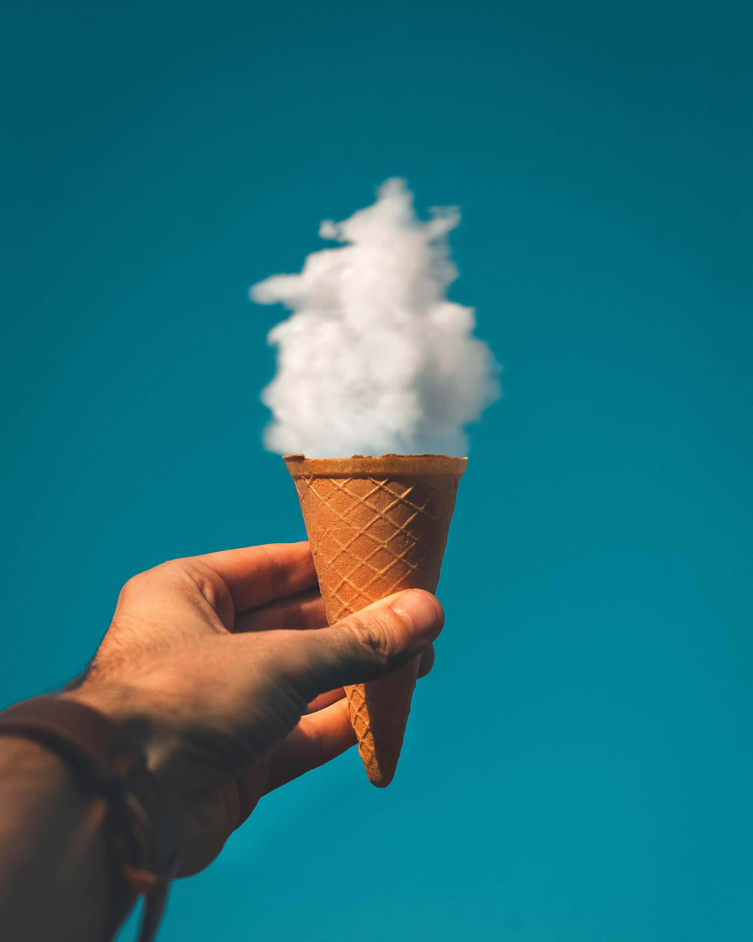 Ice Cream 桌布 壁紙 — 一隻手拿著裝滿蓬鬆白色棉花糖的鬆餅筒，背景是充滿活力的藍綠色天空。