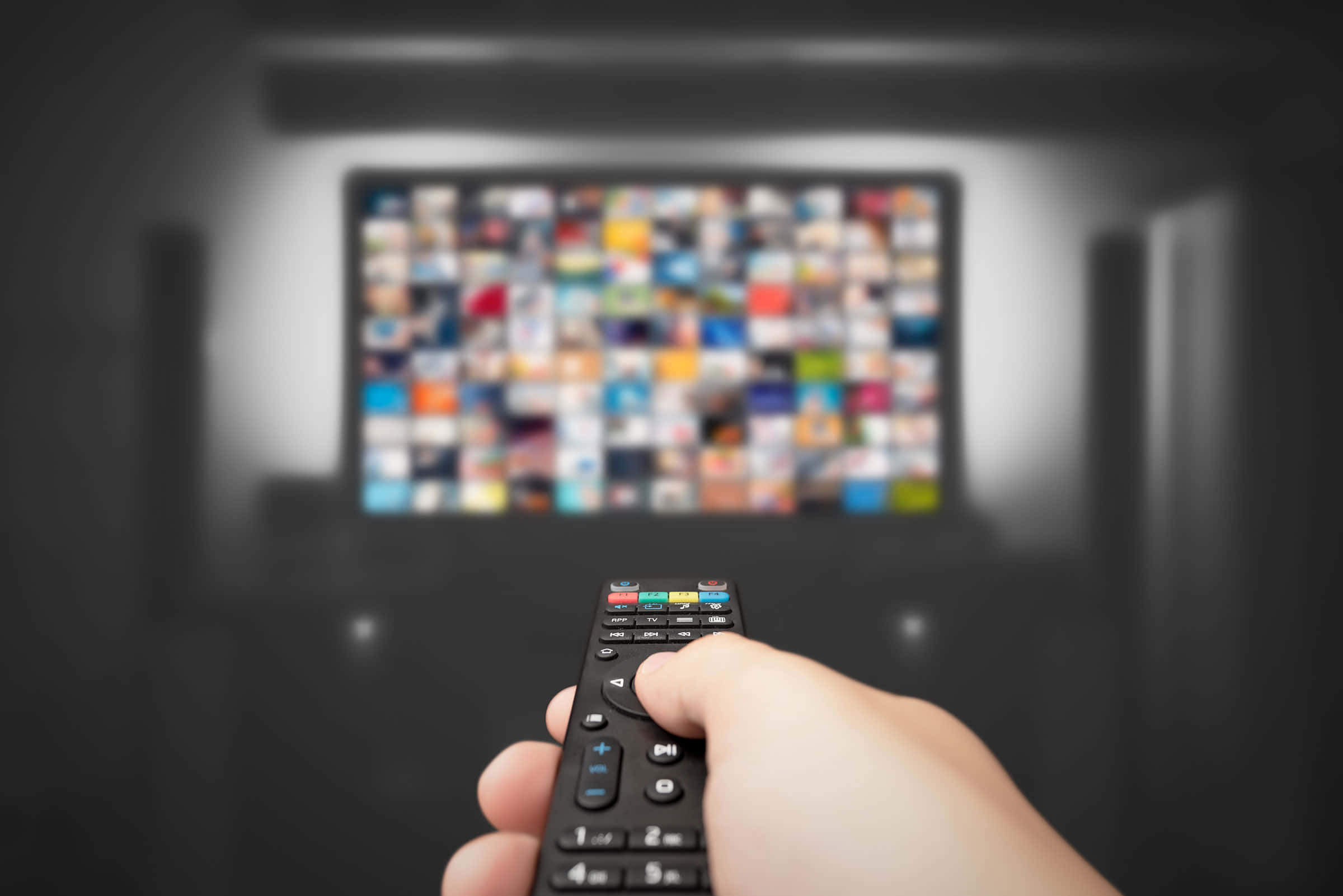 Netflix 桌布 壁紙 — 一隻手拿著遙控器，對準一個模糊的電視螢幕，螢幕上顯示著色彩繽紛的串流縮圖網格。