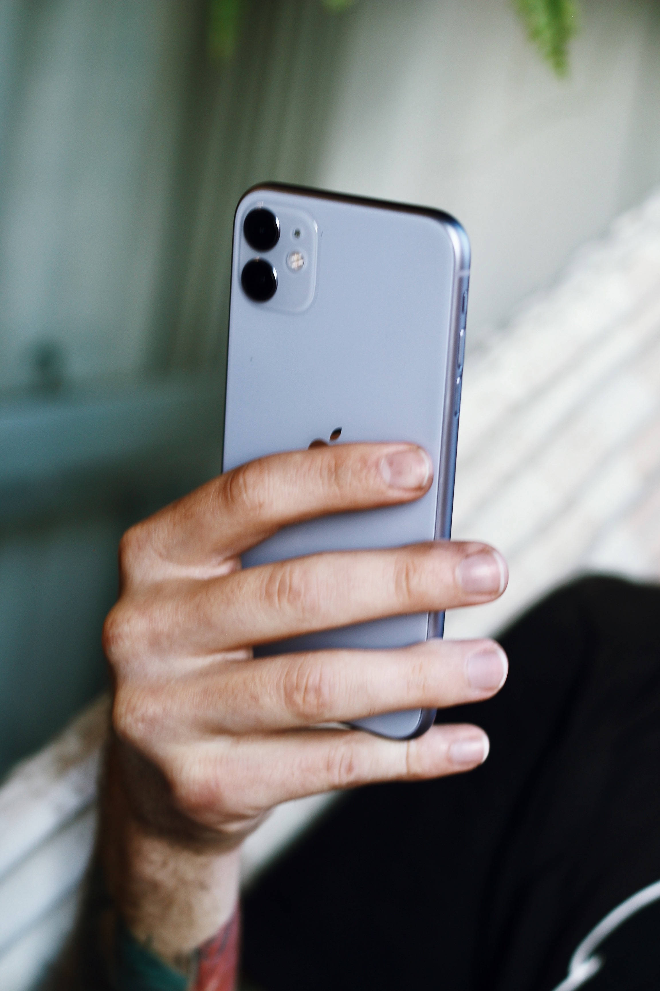 iPhone 11 桌布 壁紙 — 一隻手拿著銀色 iPhone 11，配備雙鏡頭，背景是柔和模糊的室內環境。