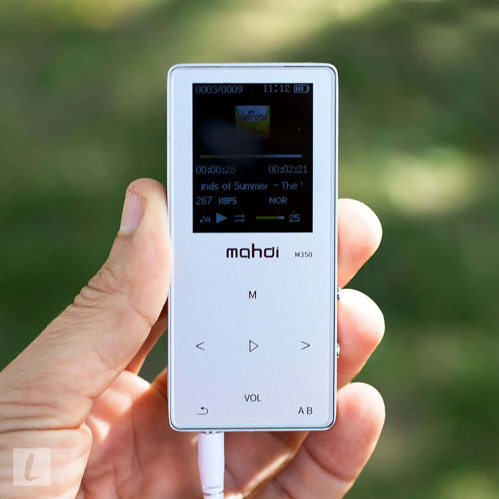 Music Player 桌布 壁紙 — 一隻手拿著銀色 Mahdi M350 MP3 播放器，在模糊的綠色戶外背景上顯示音樂播放。