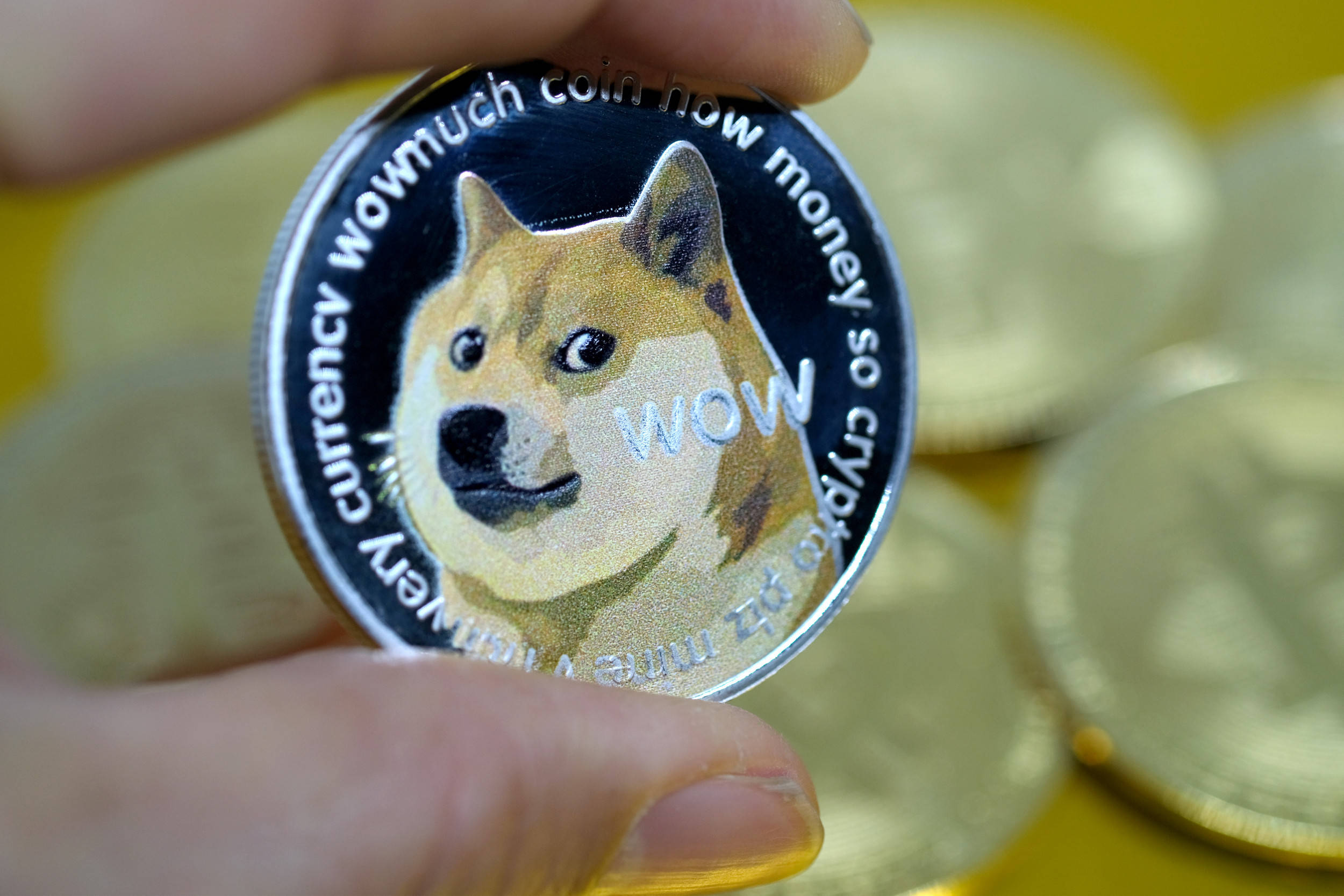 Dogecoin 桌布 壁紙 — 一隻手拿著閃亮的Dogecoin，上面有柴犬和「WOW」文字，背景是模糊的黃色其他硬幣。