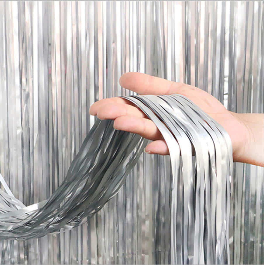 Silver Metallic 桌布 壁紙 — 一隻手拿著閃爍的銀色亮片，背景是相配的金屬流蘇。