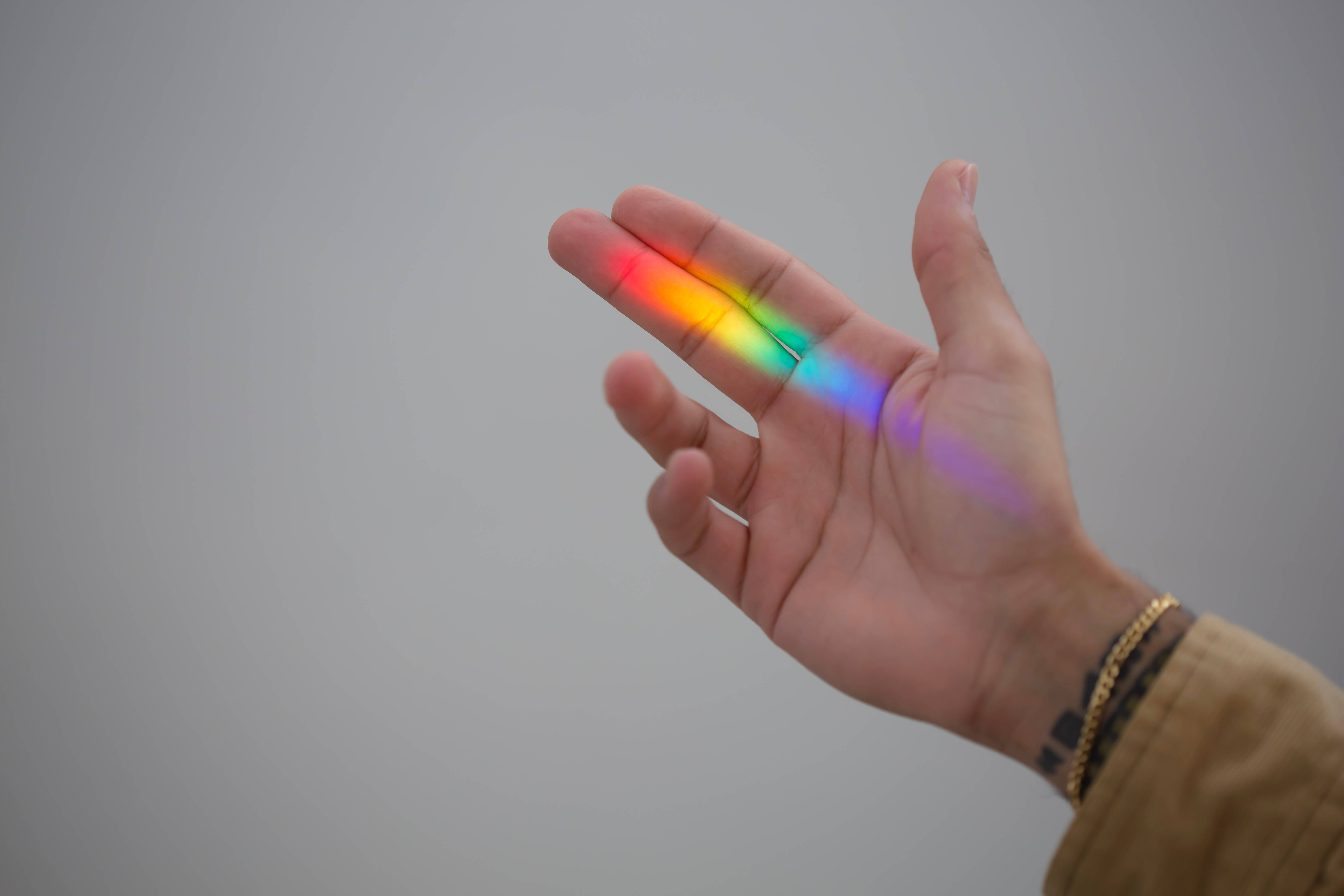 LGBT 桌布 壁紙 — 一隻手拿著鮮豔的彩虹稜鏡光，在純灰色背景上將彩色光譜投射到手掌上。