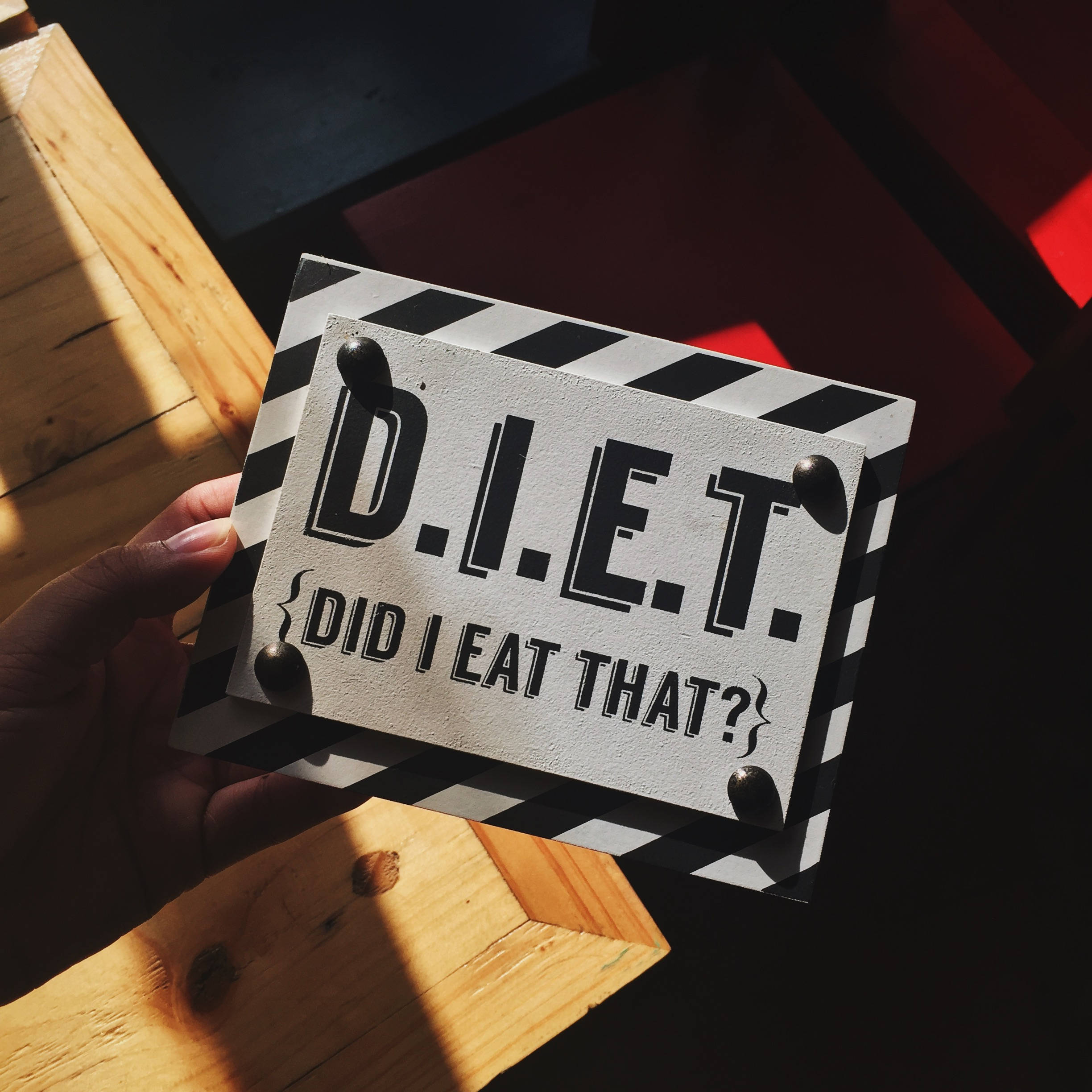 meme 桌布 壁紙 — 一隻手拿著黑白場記板，上面有 'D.I.E.T. DID I EAT THAT?' 文字，背景是木質和紅色幾何陰影。