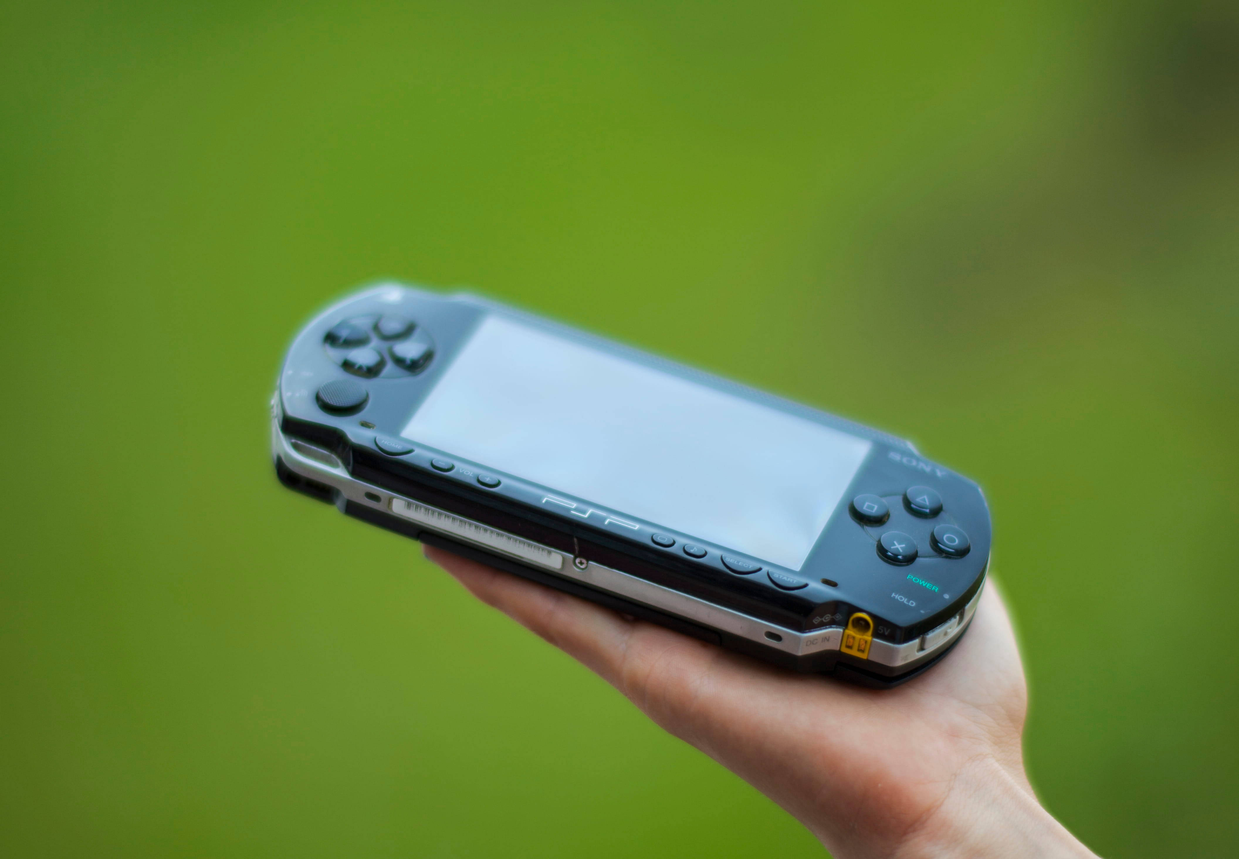 PlayStation 桌布 壁紙 — 一隻手拿著黑色Sony PSP掌上型遊戲機，背景是柔和的綠色模糊效果。