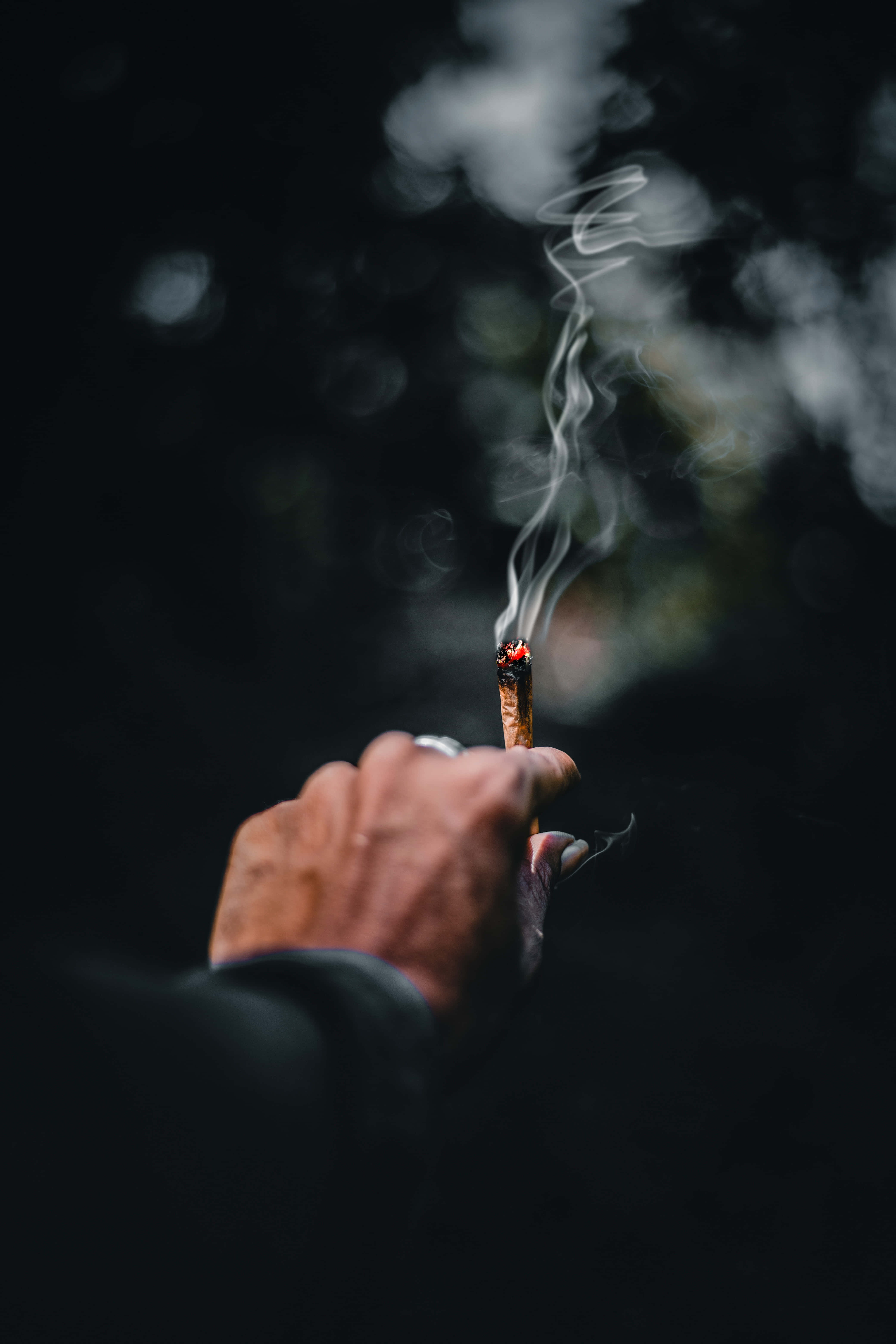 超炫動圖 桌布 壁紙 — 一隻手拿著點燃的香煙，背景模糊黑暗，煙霧向上繚繞。