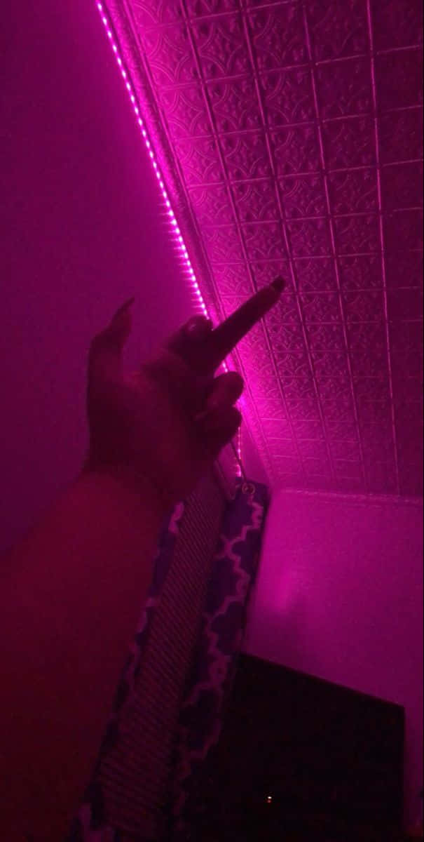 桌布 壁紙 — 一隻手指向上，指向一條發光的粉紅色LED燈帶，照亮了昏暗房間內有紋理的天花板。