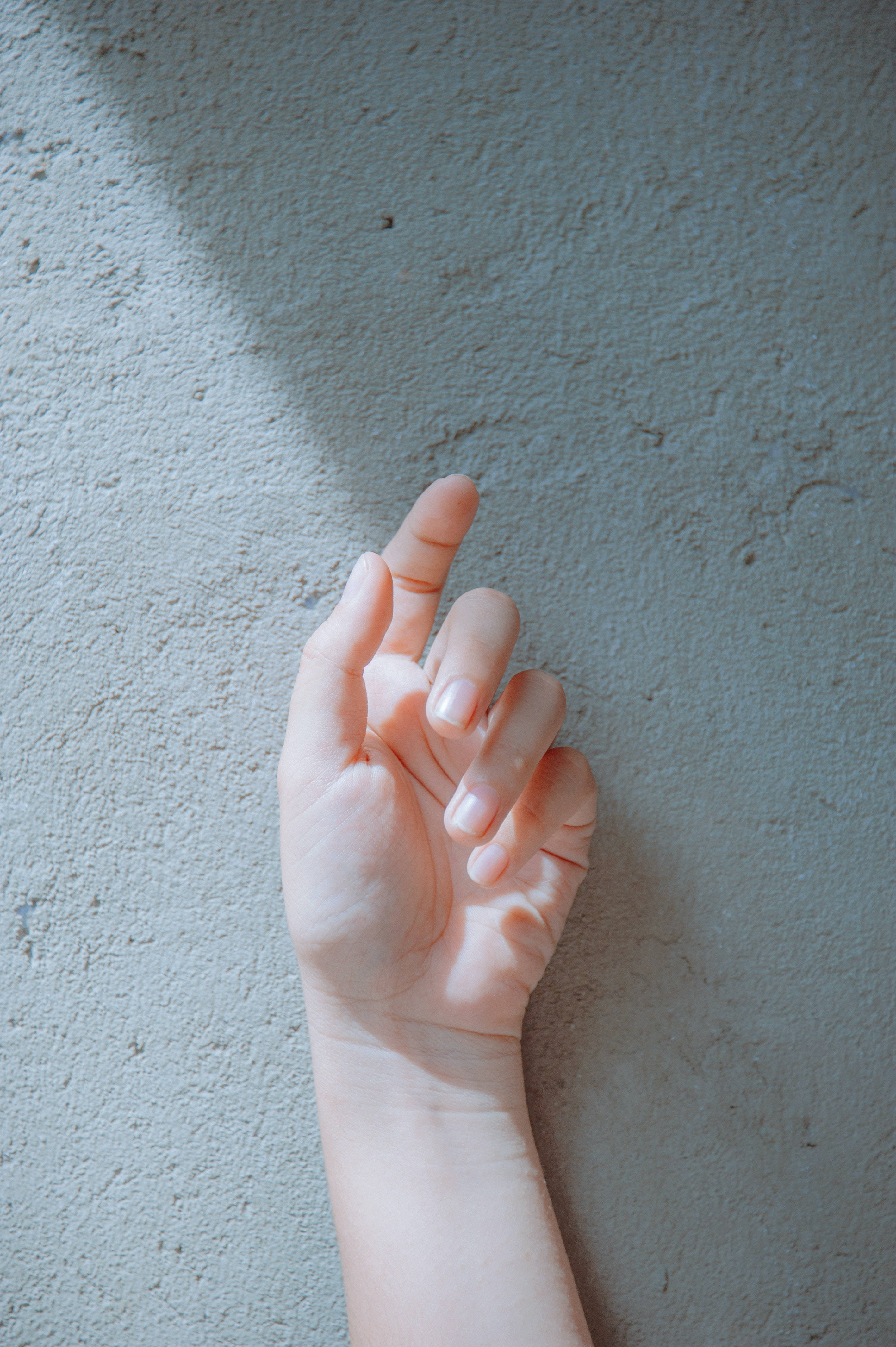 hands 桌布 壁紙 — 一隻手指微微彎曲的手靠在紋理灰色牆上，沐浴在柔和自然光中。