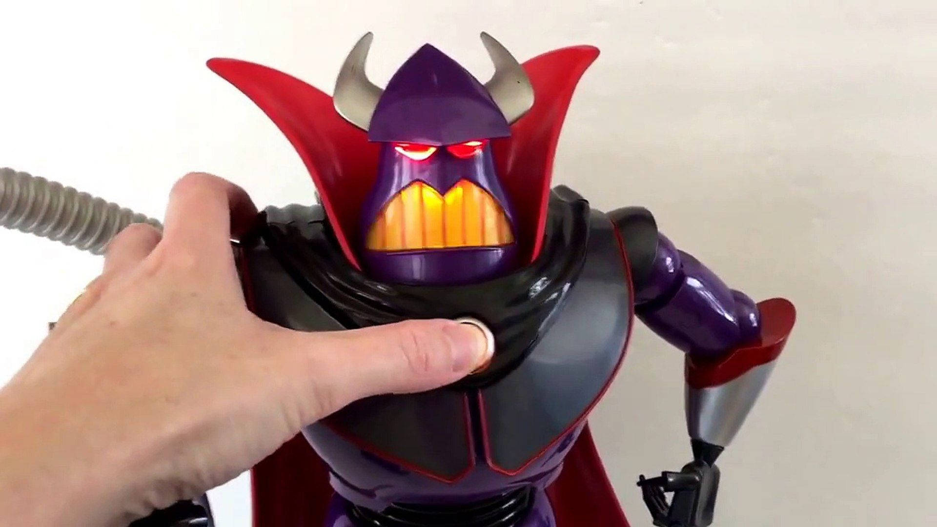 emperor zurg 桌布 壁紙 — 一隻手按下一個紫色和紅色的邪惡機器人玩具上的按鈕，該玩具擁有發光的紅色眼睛和猙獰的笑容。