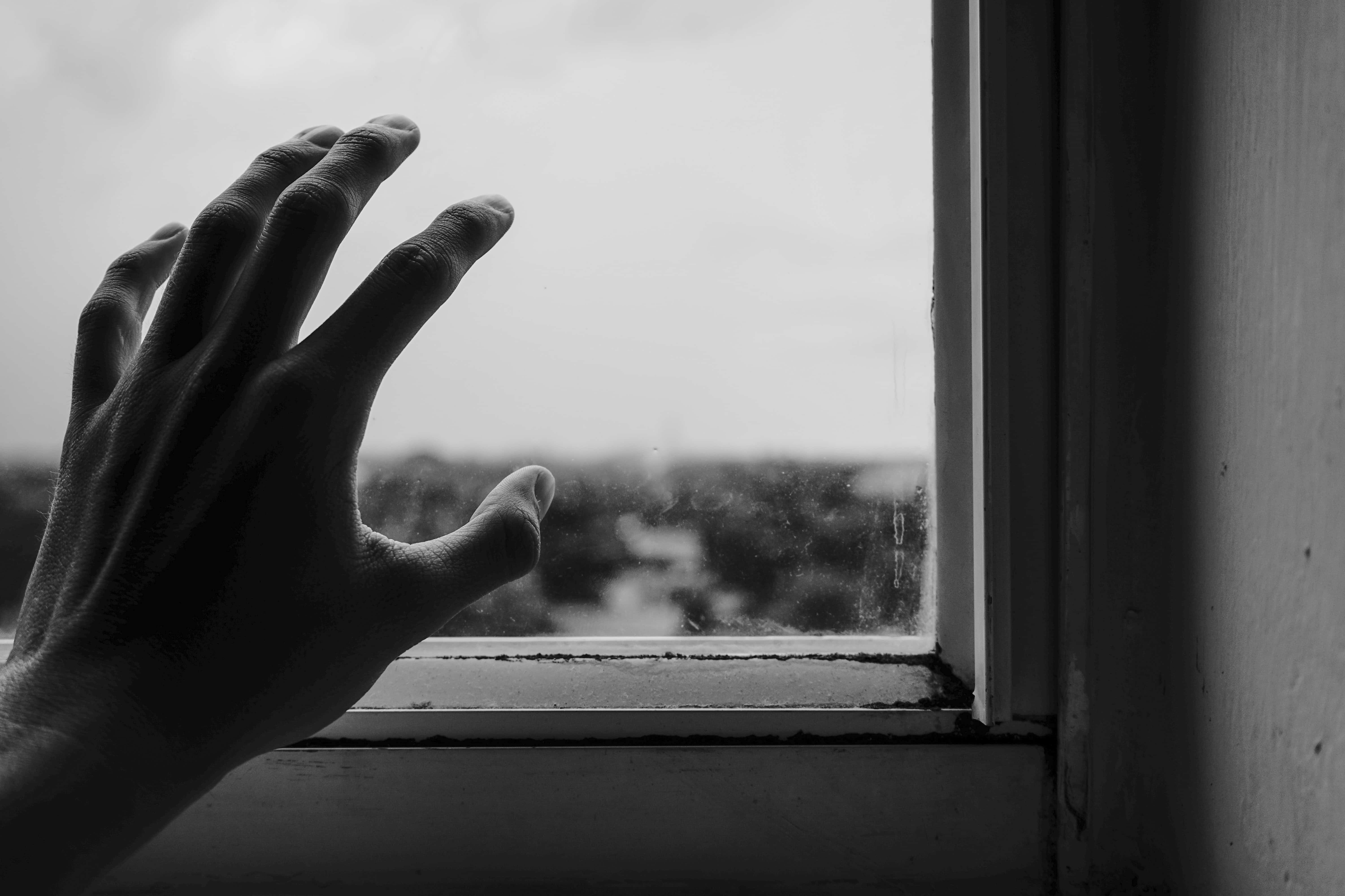 Gloomy 桌布 壁紙 — 一隻手按在佈滿灰塵的窗玻璃上，黑白畫面，凝視著模糊的城市景觀。