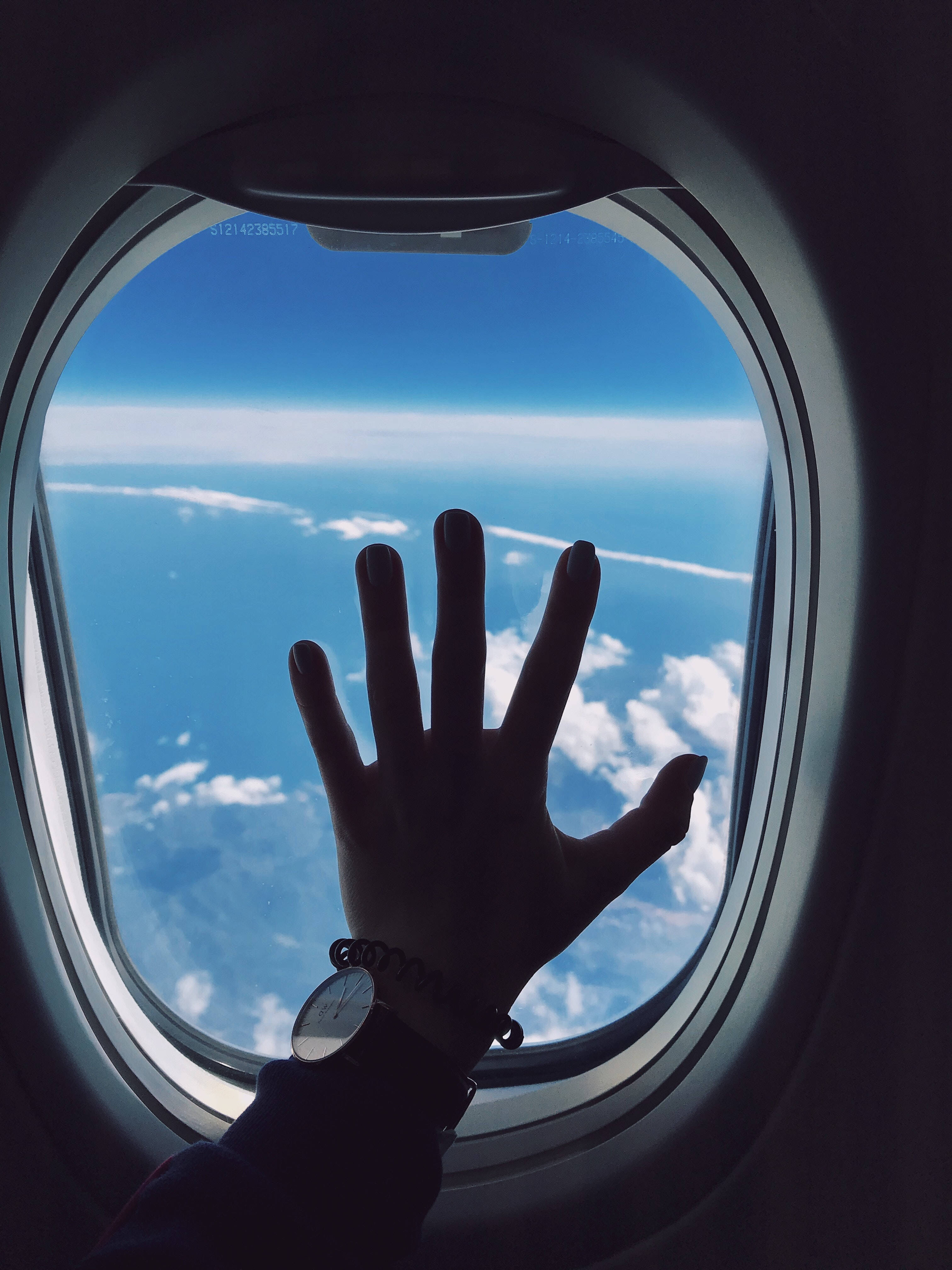 wanderlust 桌布 壁紙 — 一隻手按在飛機窗上，展現出下方廣闊的藍天和蓬鬆的白雲。