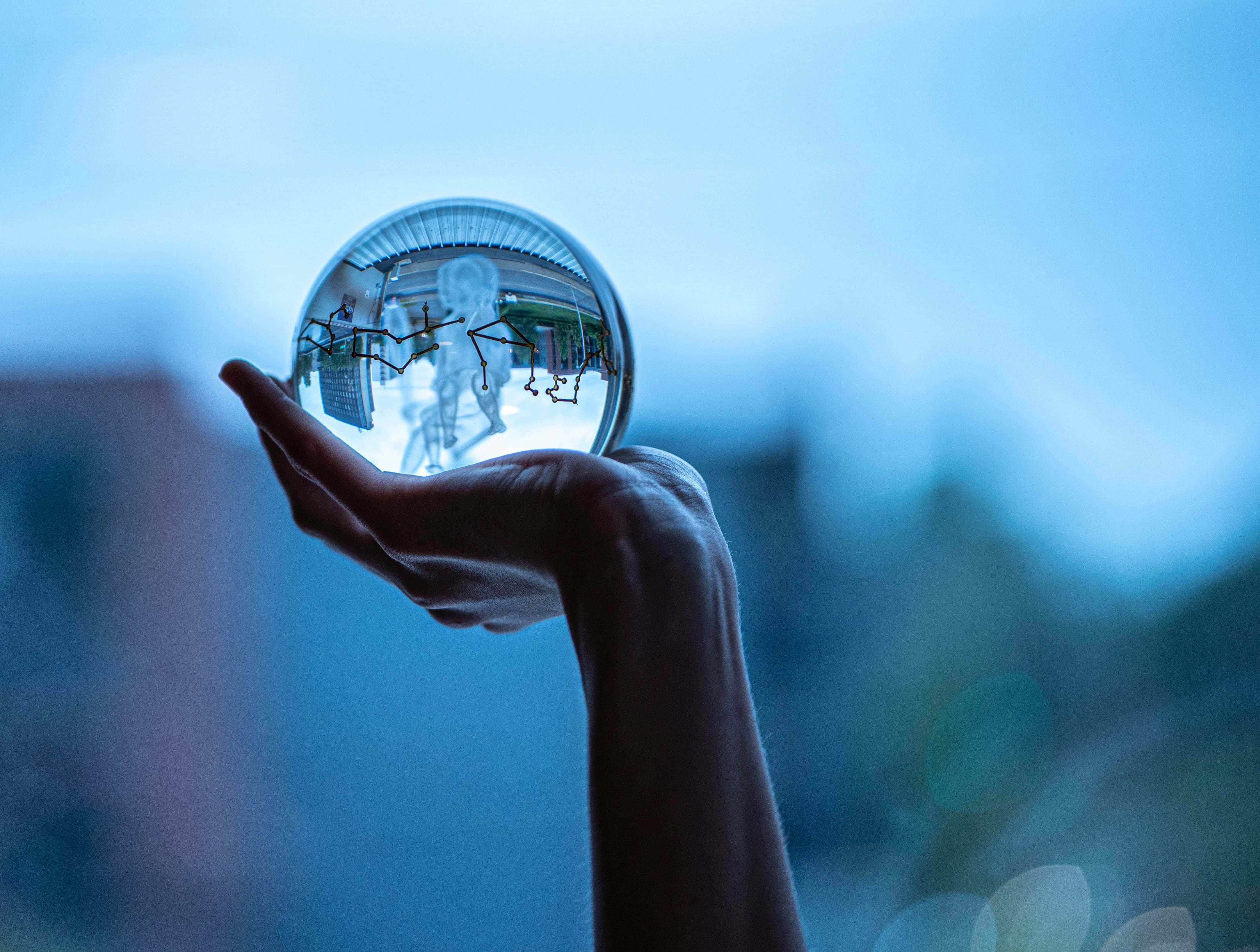 Crystal Ball 桌布 壁紙 — 一隻手捧著一個反射的水晶球，顯示出一個微縮的城市景觀，背景是柔和的藍天。