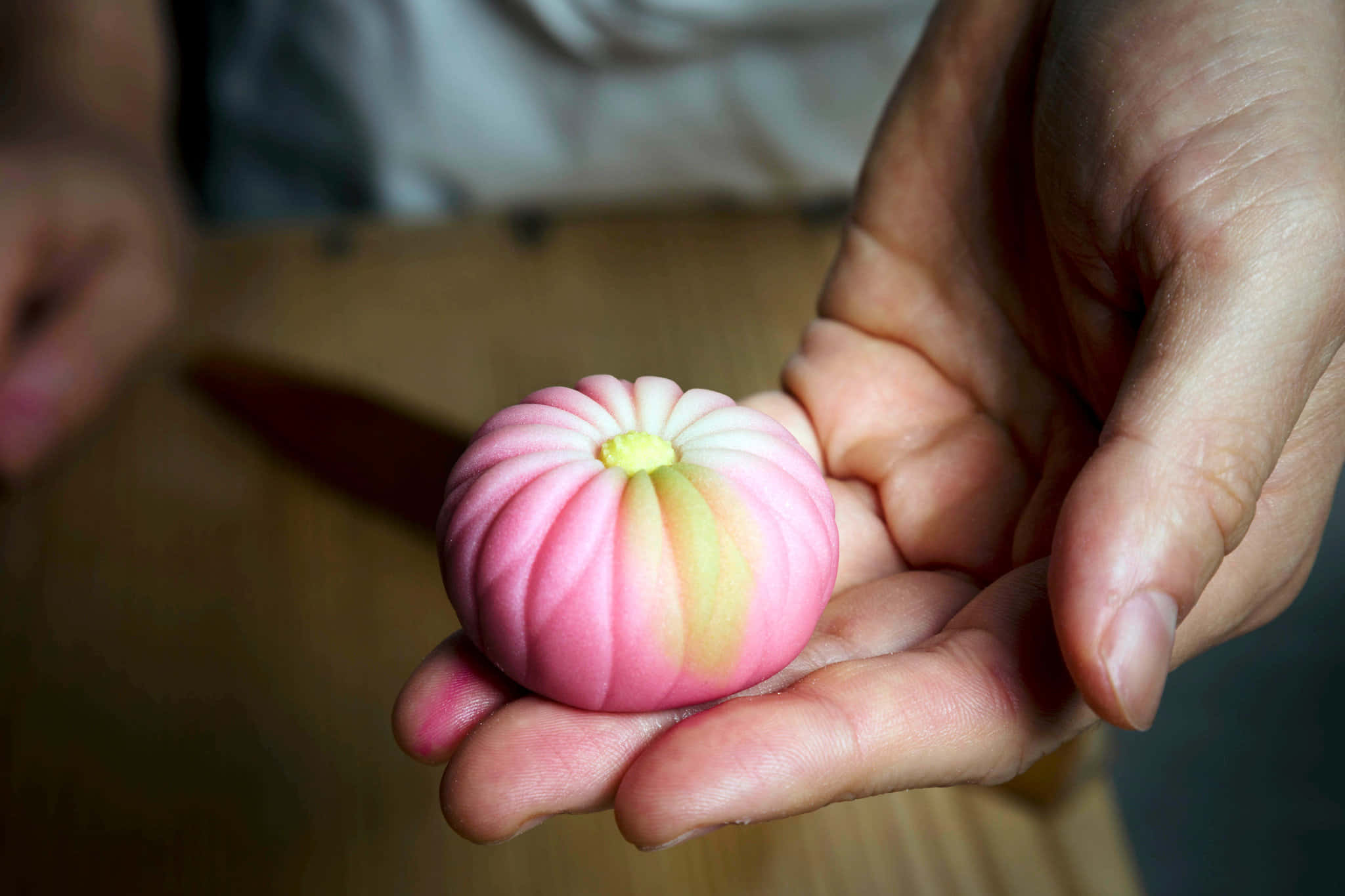 Japanese Sweets 桌布 壁紙 — 一隻手捧著精緻的粉黃色分層日式麻糬甜點，背景柔和。