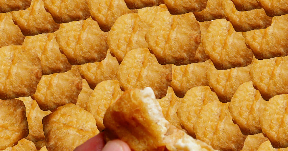 Chicken Nuggets 桌布 壁紙 — 一隻手掰開金黃色的炸雞塊，露出柔軟的白色內部，周圍是類似的雞塊海洋。
