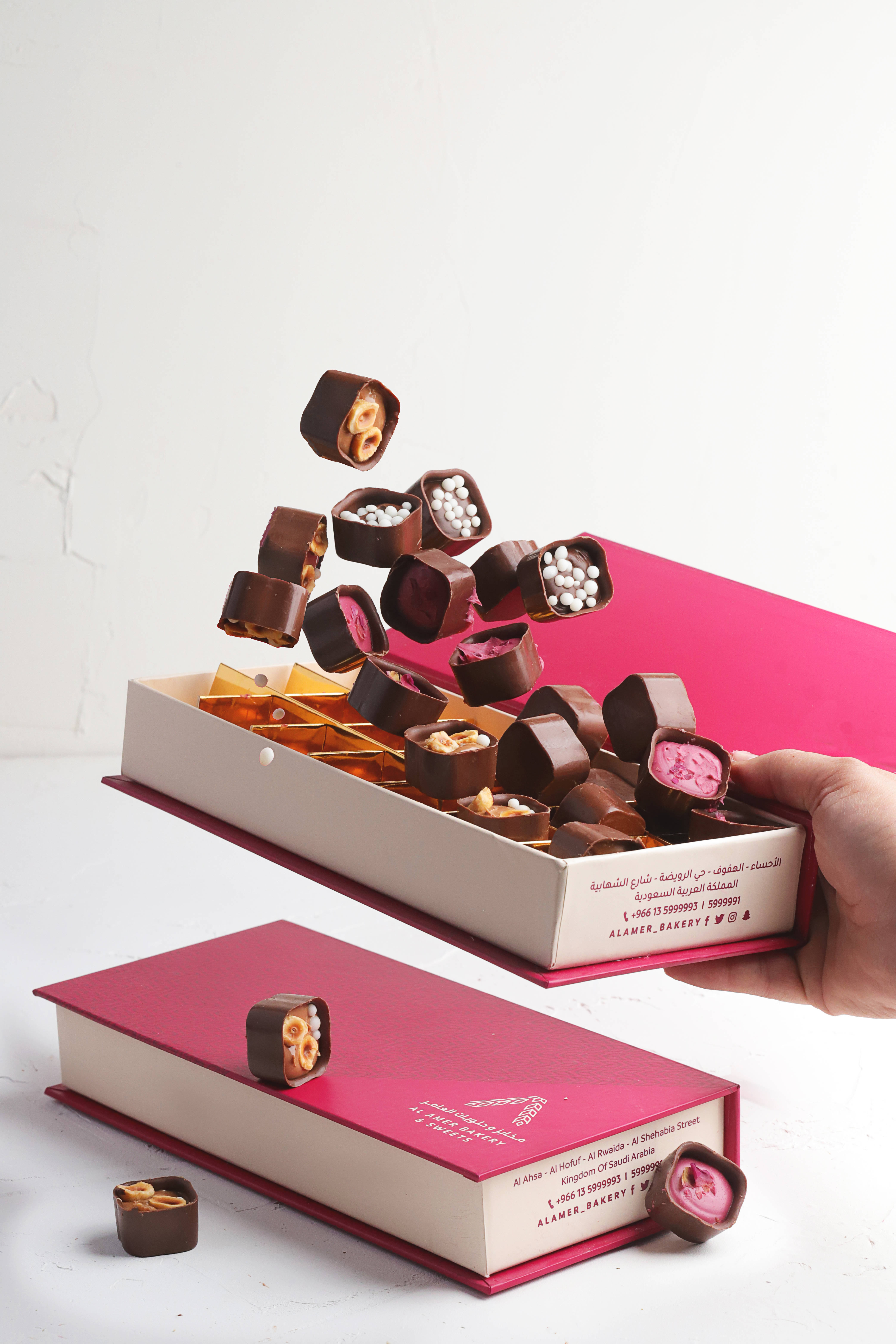 Chocolate 桌布 壁紙 — 一隻手提起一個粉紅色盒子，各種巧克力在空中爆發，形成動態瀑布，背景是潔淨的白色。