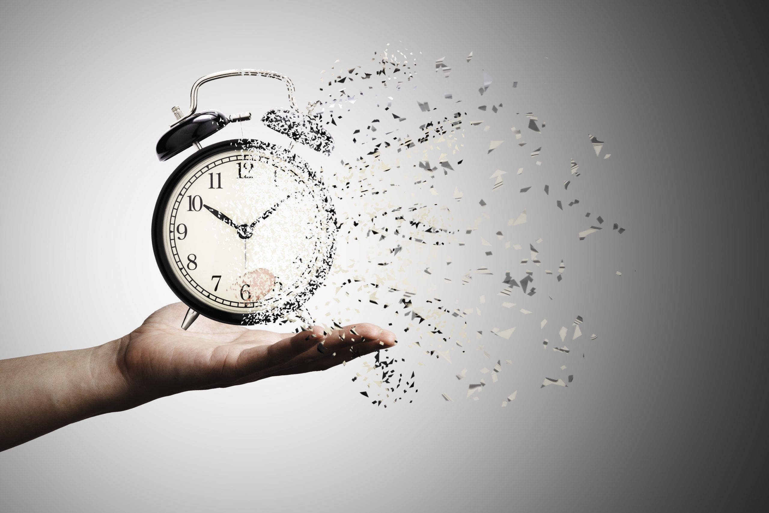 times up 桌布 壁紙 — 一隻手握住一個正在碎裂的黑色鬧鐘，碎片在灰色背景上向外爆開。