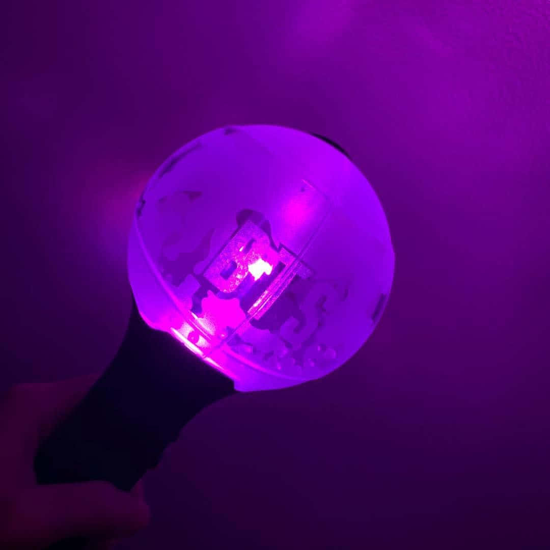 Bts Army Bomb 桌布 壁紙 — 一隻手握住一個發光的紫色LED燈棒，帶有半透明球體，在黑暗背景下投射出鮮豔的紫色光芒。